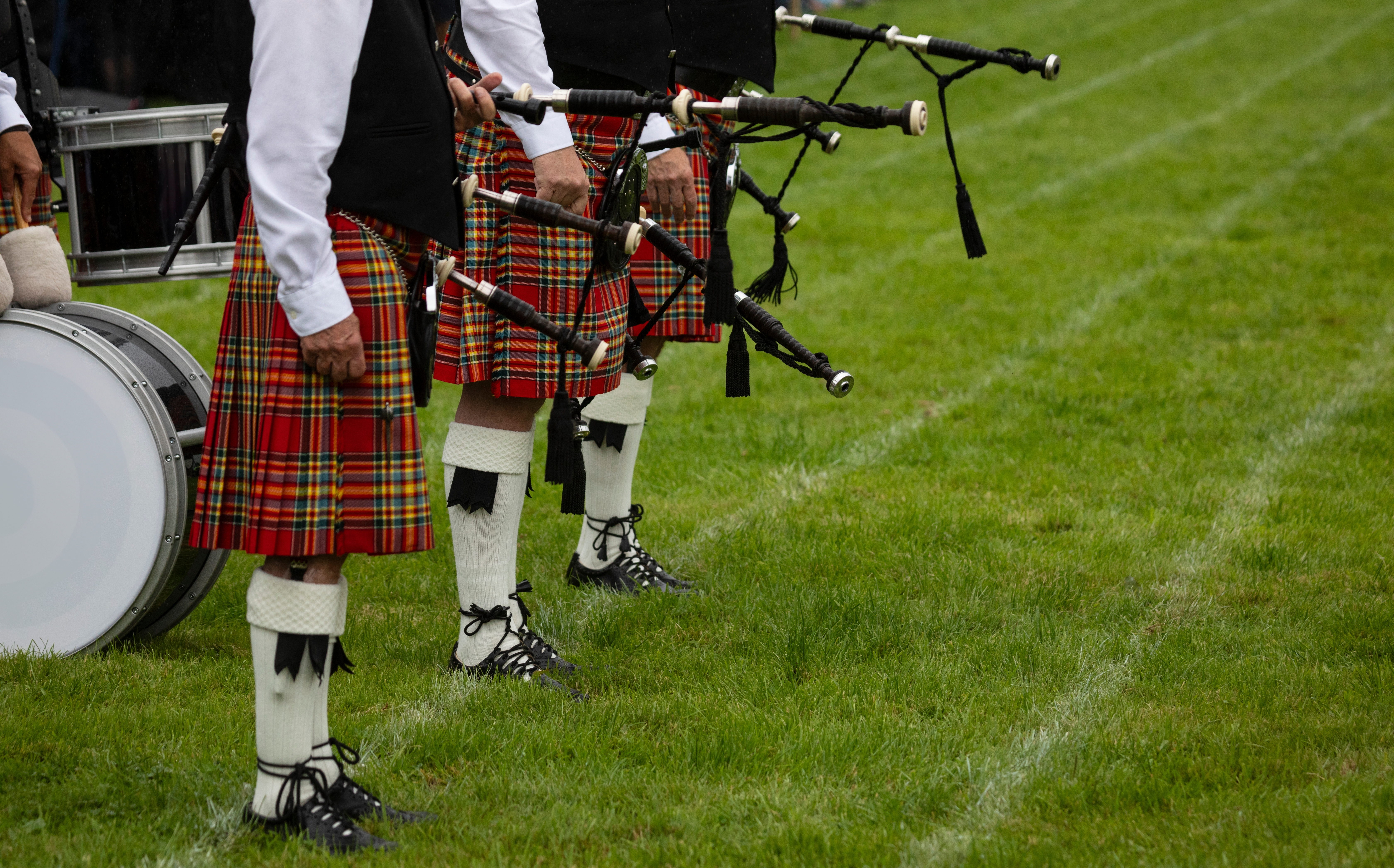 Imponerende skotsk sækkepibeorkester i røde tartan-kilte, hvide knæstrømper og sorte veste, klar til optræden ved det traditionsrige Highland Games i Crieff, Skotland.