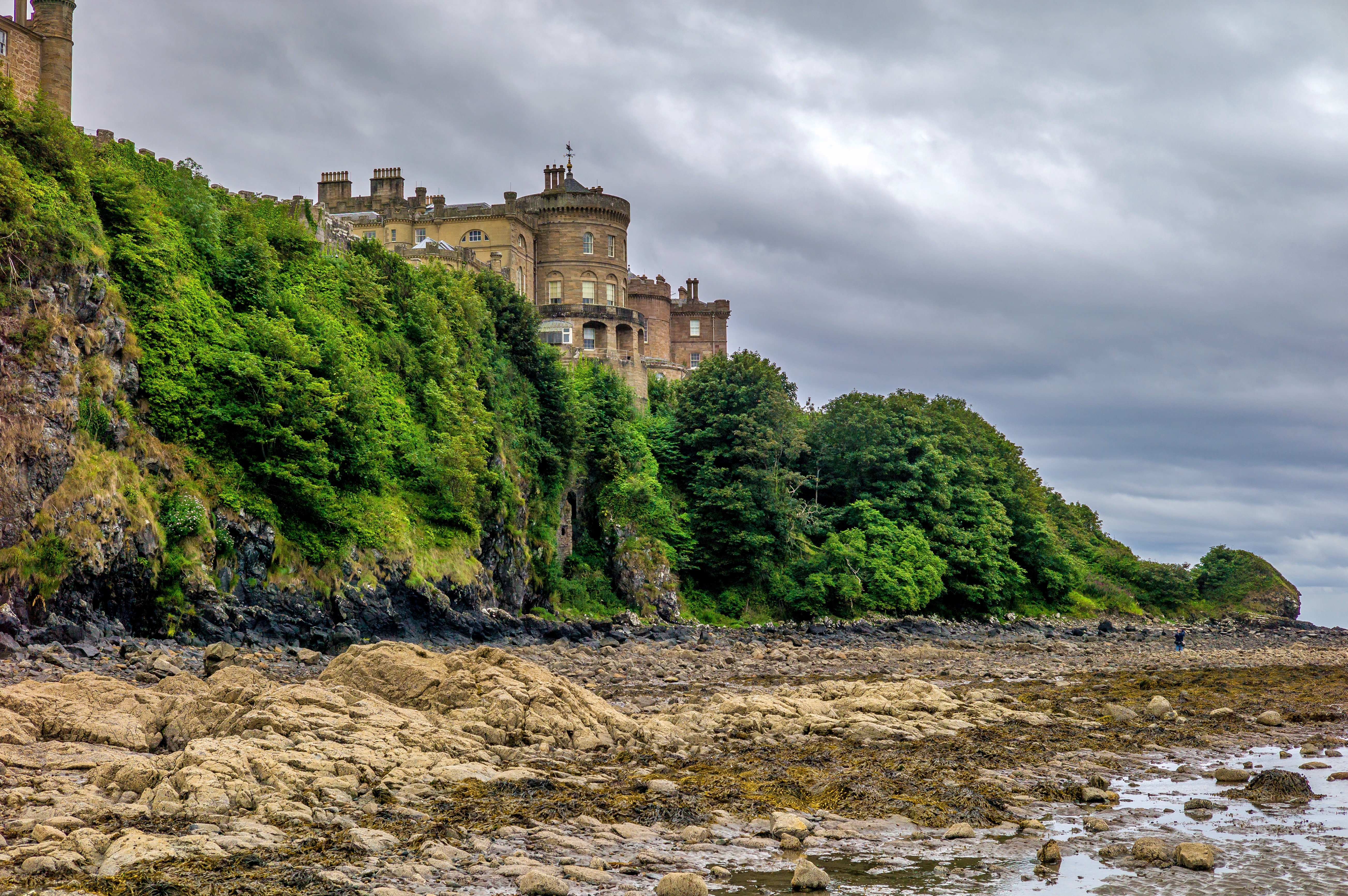 Culzean Castle ved kysten i Skotland omgivet af grønne træer og dramatiske klippeformationer ved lavvande