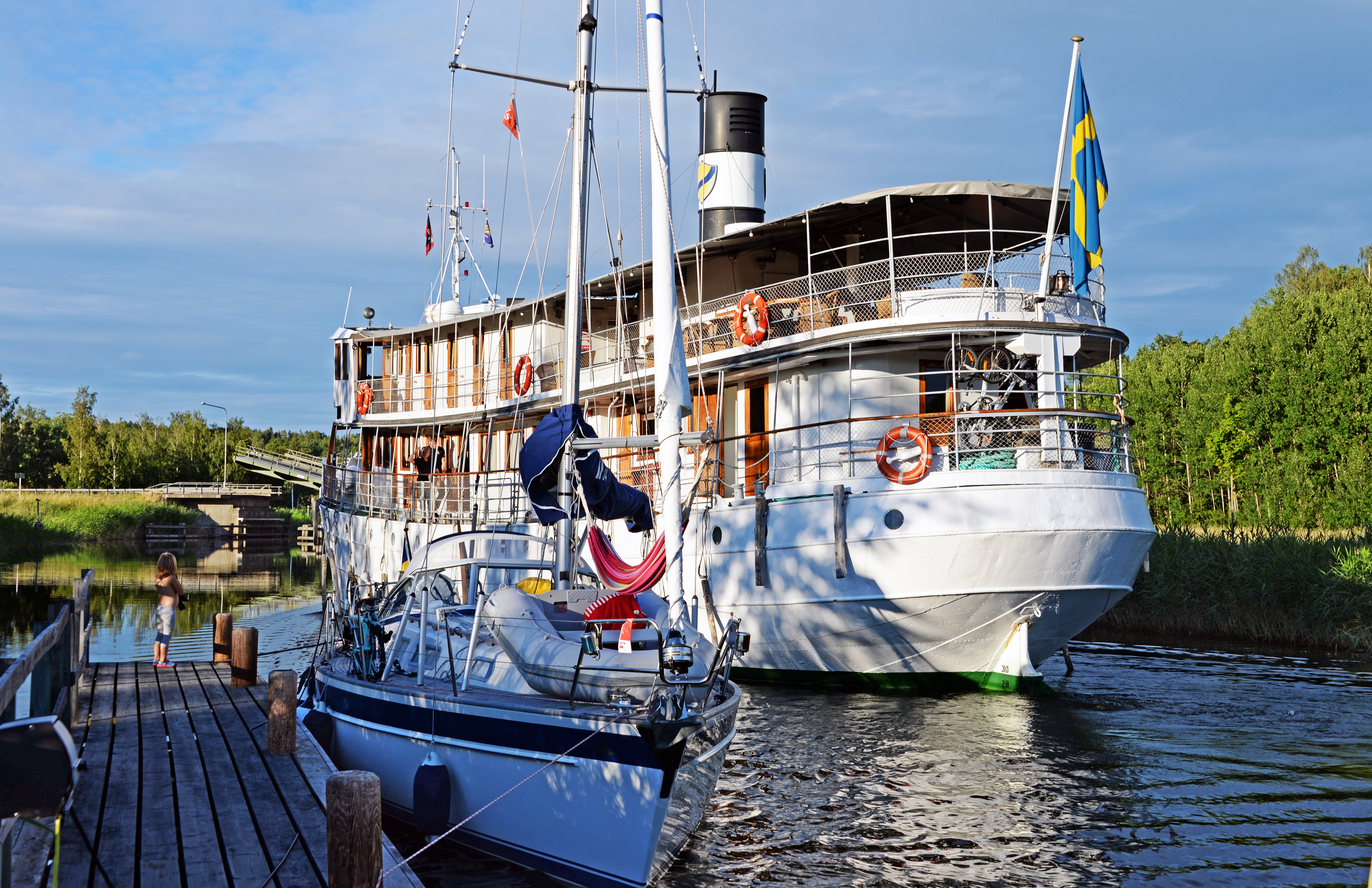 Smuk klassisk dampbåd og sejlbåd ved Göta Kanal i Sverige på en dejlig sommerdag med svensk flag vajende i vinden