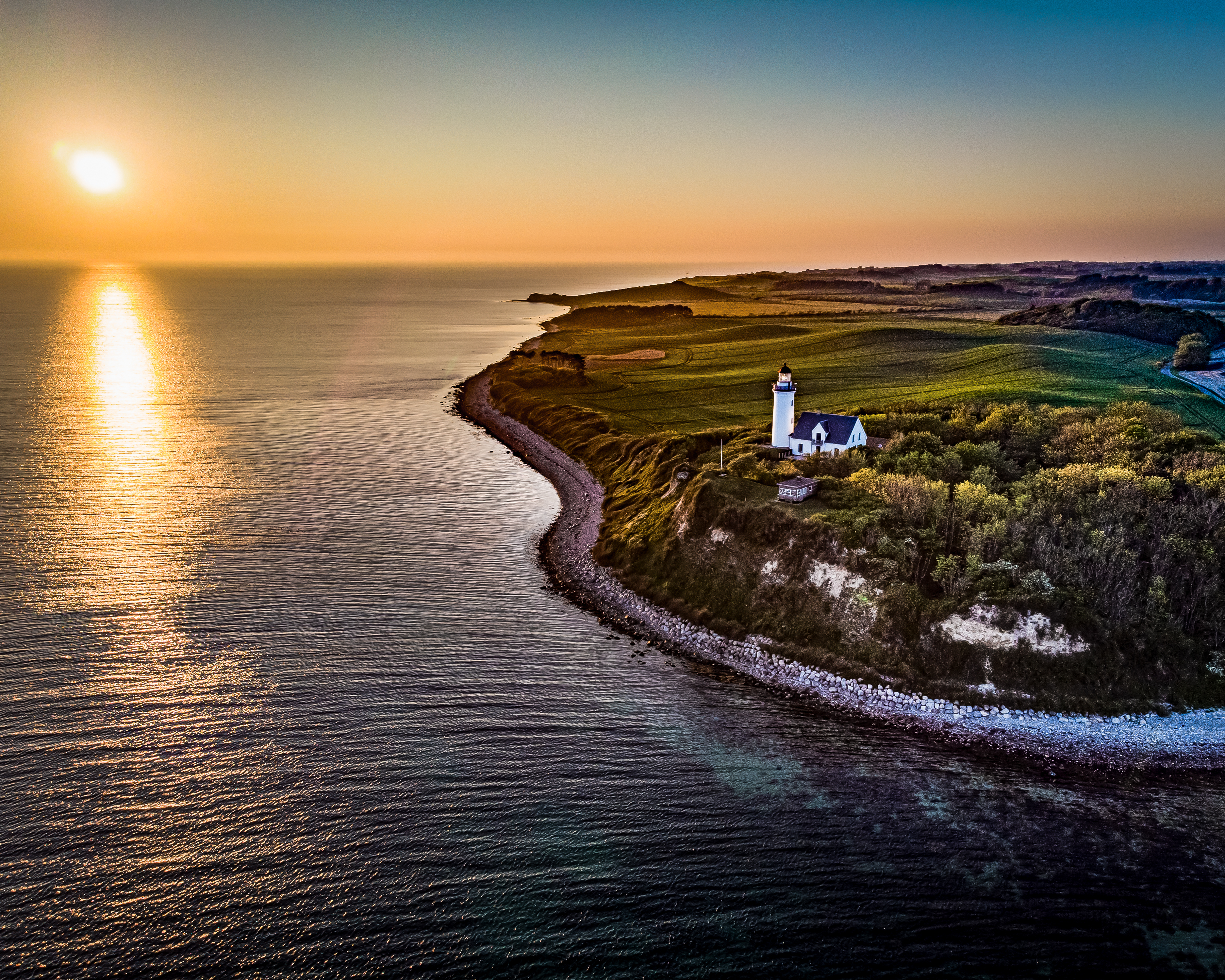 Hvidt fyrtårn på dansk klint med gylden solnedgang og blåt hav