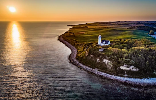 Hvidt fyrtårn på dansk klint med gylden solnedgang og blåt hav
