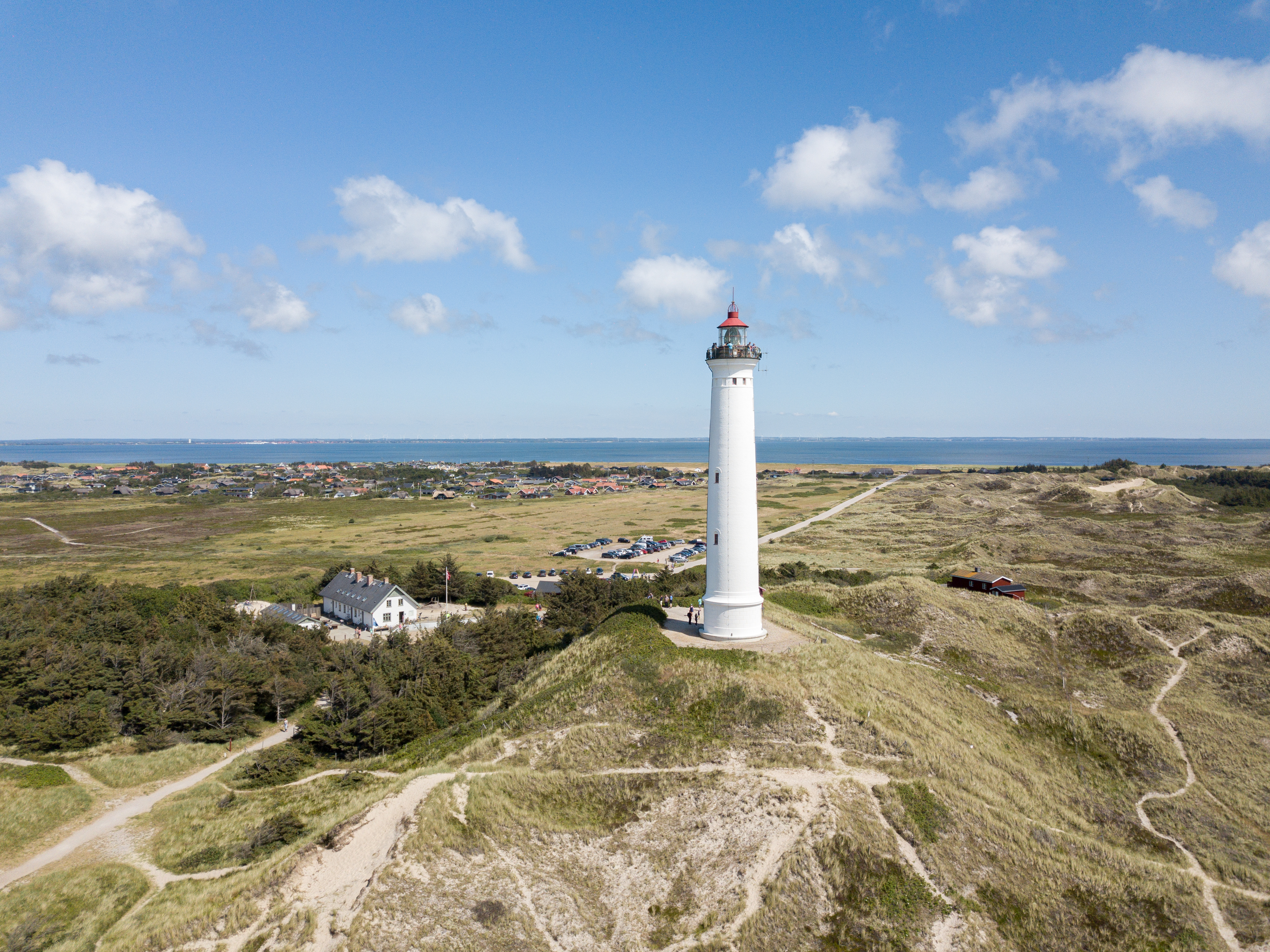 Dansk fyrtårn ved kysten omgivet af klitlandskab under sommerhimmel