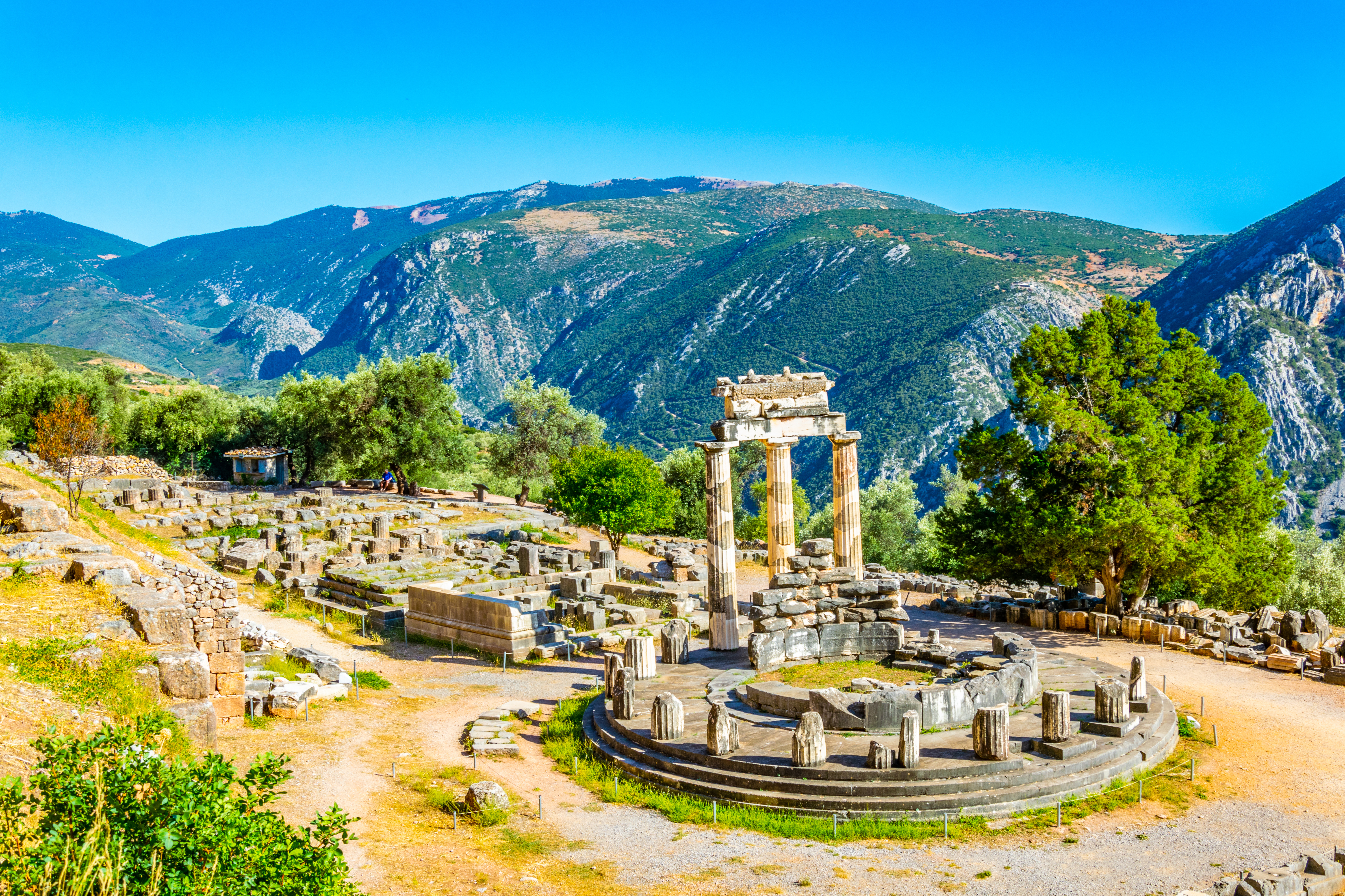 Smukke antikke ruiner ved Athena Pronaia-helligdommen i Delphi, Grækenland, med tre stående søjler og UNESCO-beskyttet arkæologisk site omgivet af grønne bjerge
