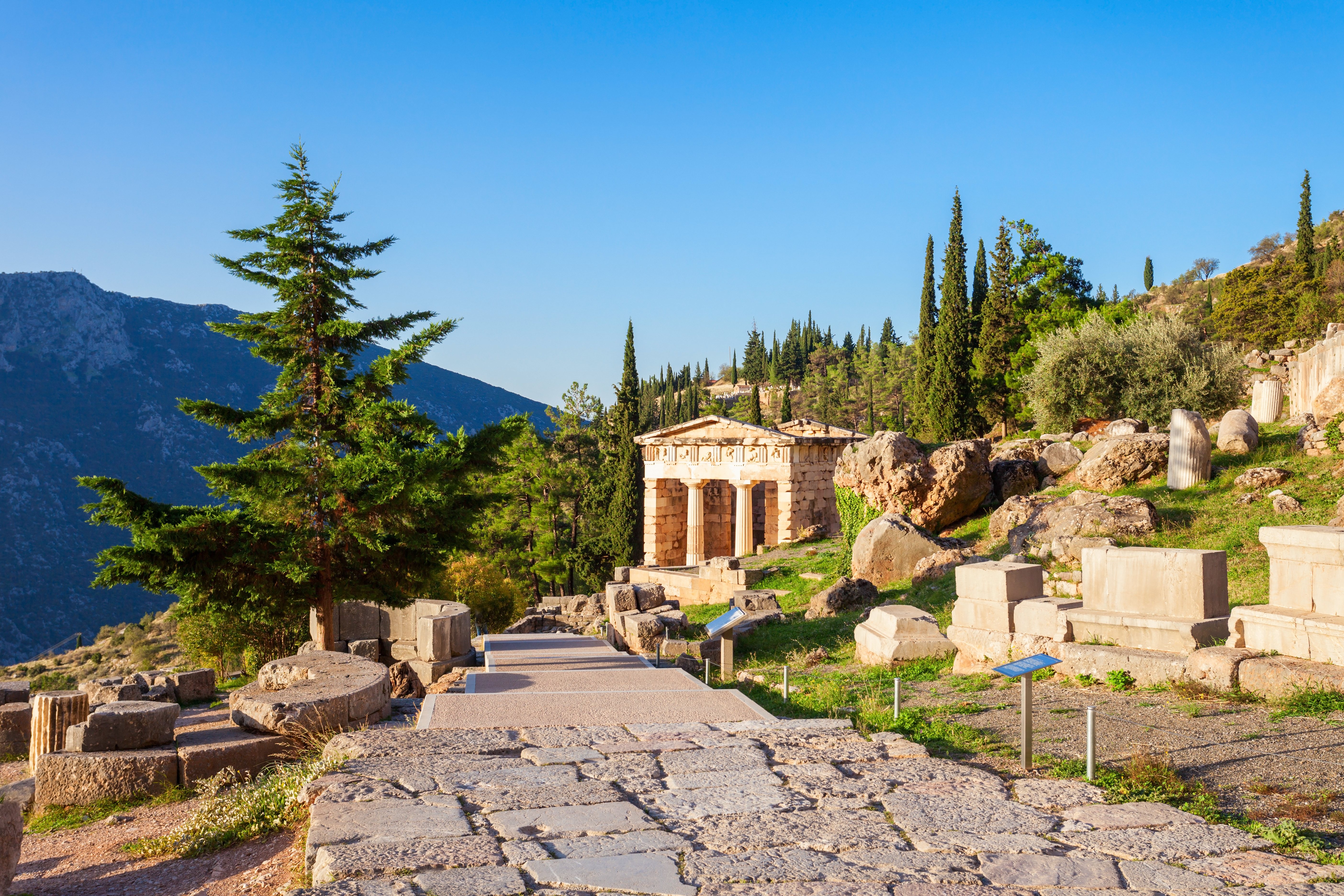 Historiske ruiner i Delphi, Grækenland, med det smukke Athenernes skatkammer, doriske søjler og antikke stenmure omgivet af natur og bjerge