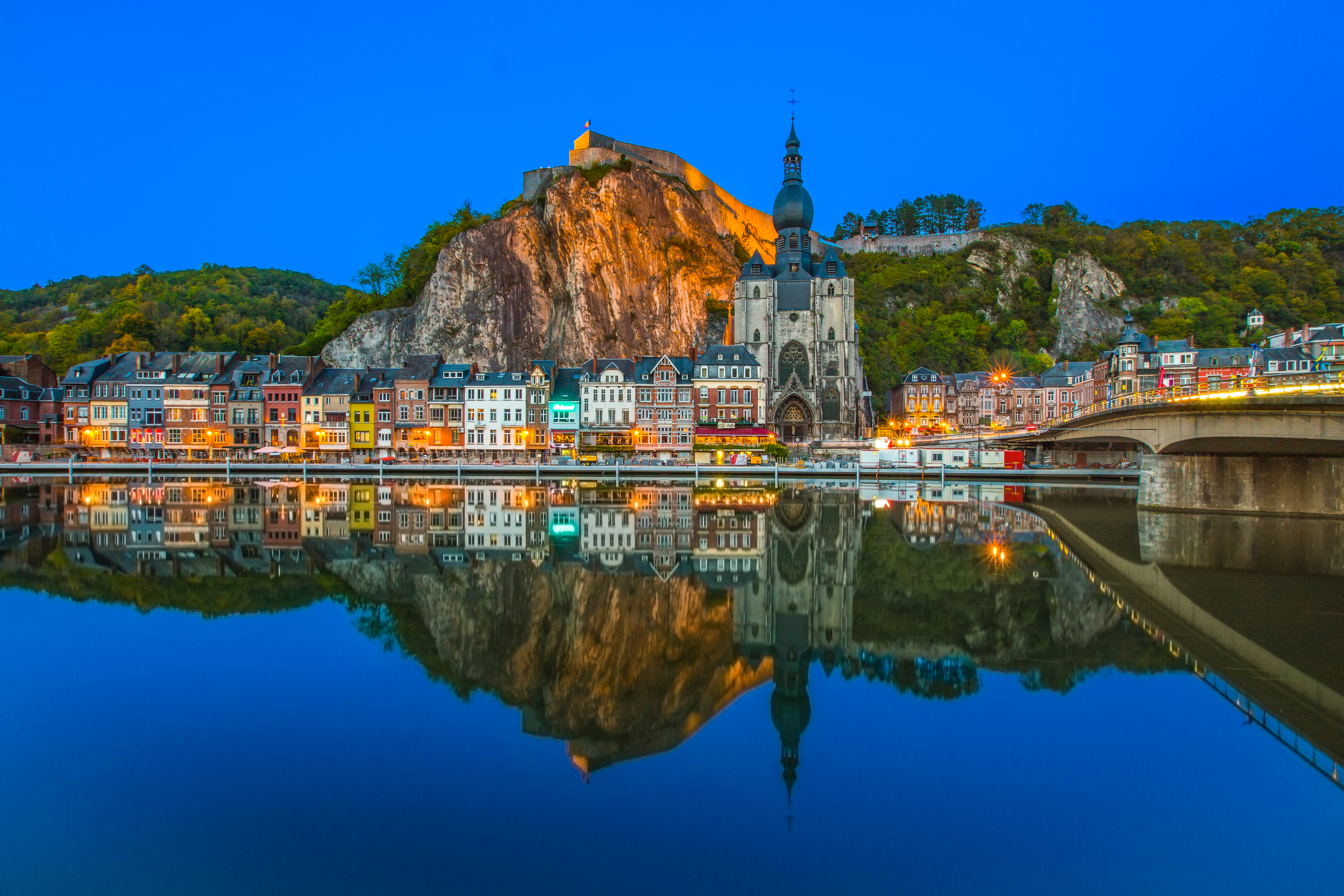 Magisk aftenstemning i Dinant, Belgien, med det oplyste citadel på klippen, kirken og de farverige huse reflekteret i Meuse-floden
