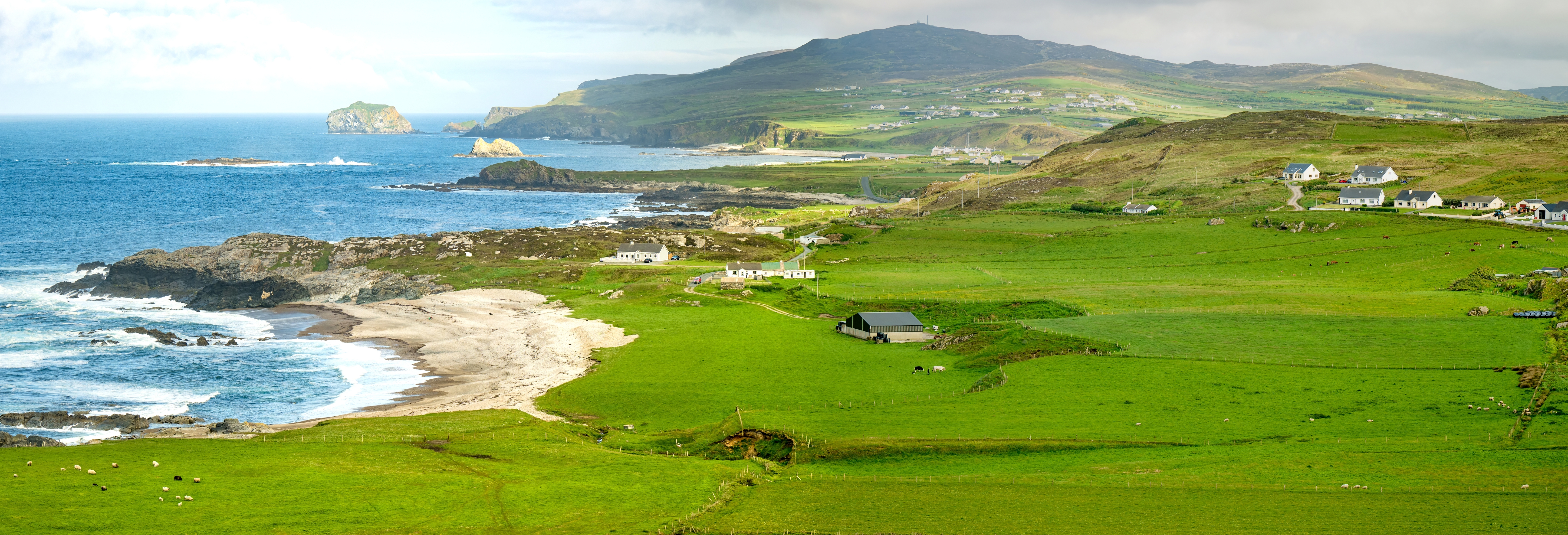 Storslået udsigt over Irlands nordligste punkt Malin Head i Donegal med grønne marker, sandstrand og det blå Atlanterhav