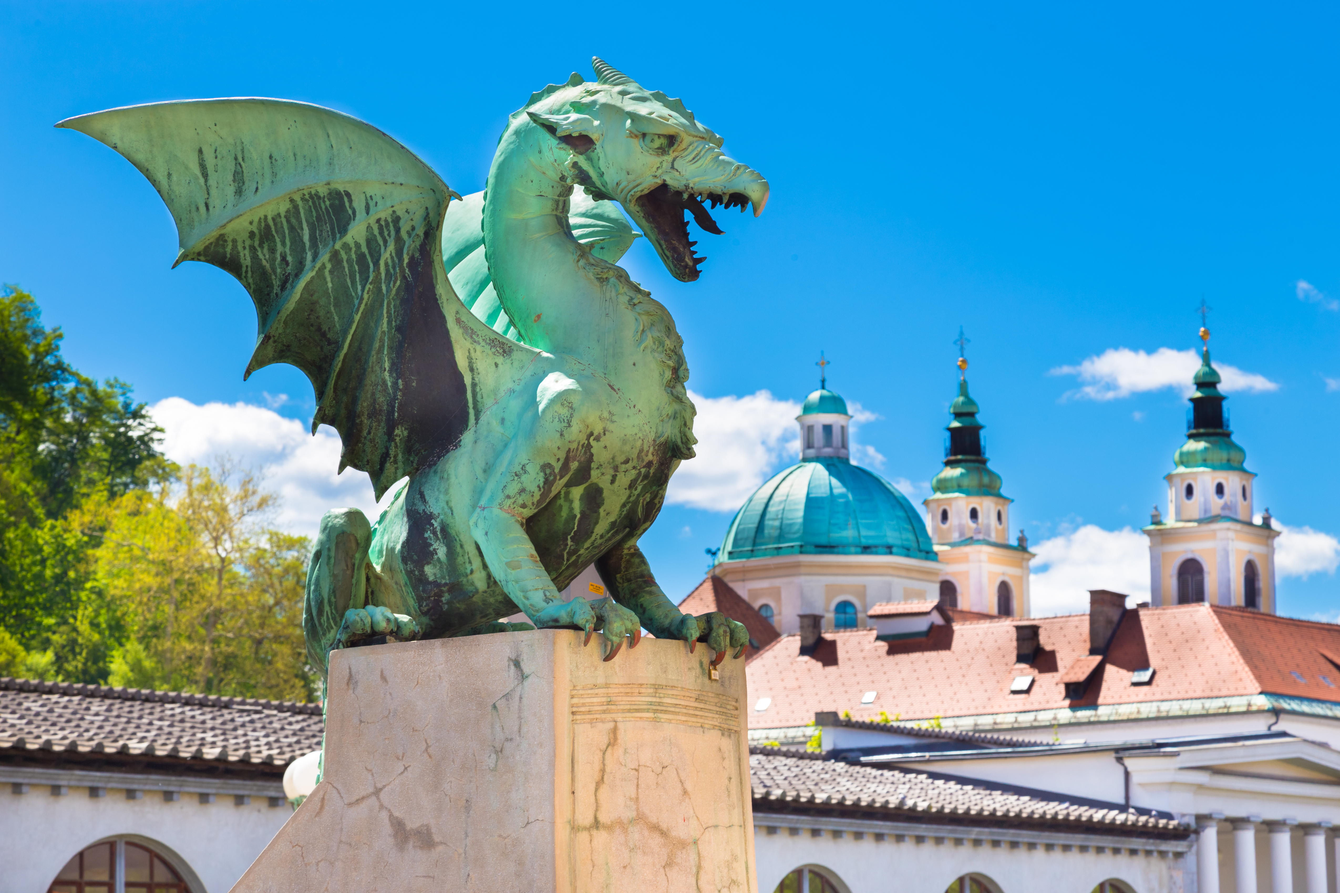 Den majestætiske drage på Ljubljanas berømte Dragebro med byens historiske kupler og tårne i baggrunden, et symbol på Sloveniens rige kulturarv.