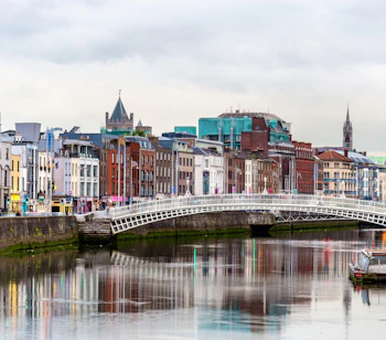 Historisk Ha'penny Bridge over River Liffey med Dublins farverige bybillede i baggrunden, Irland