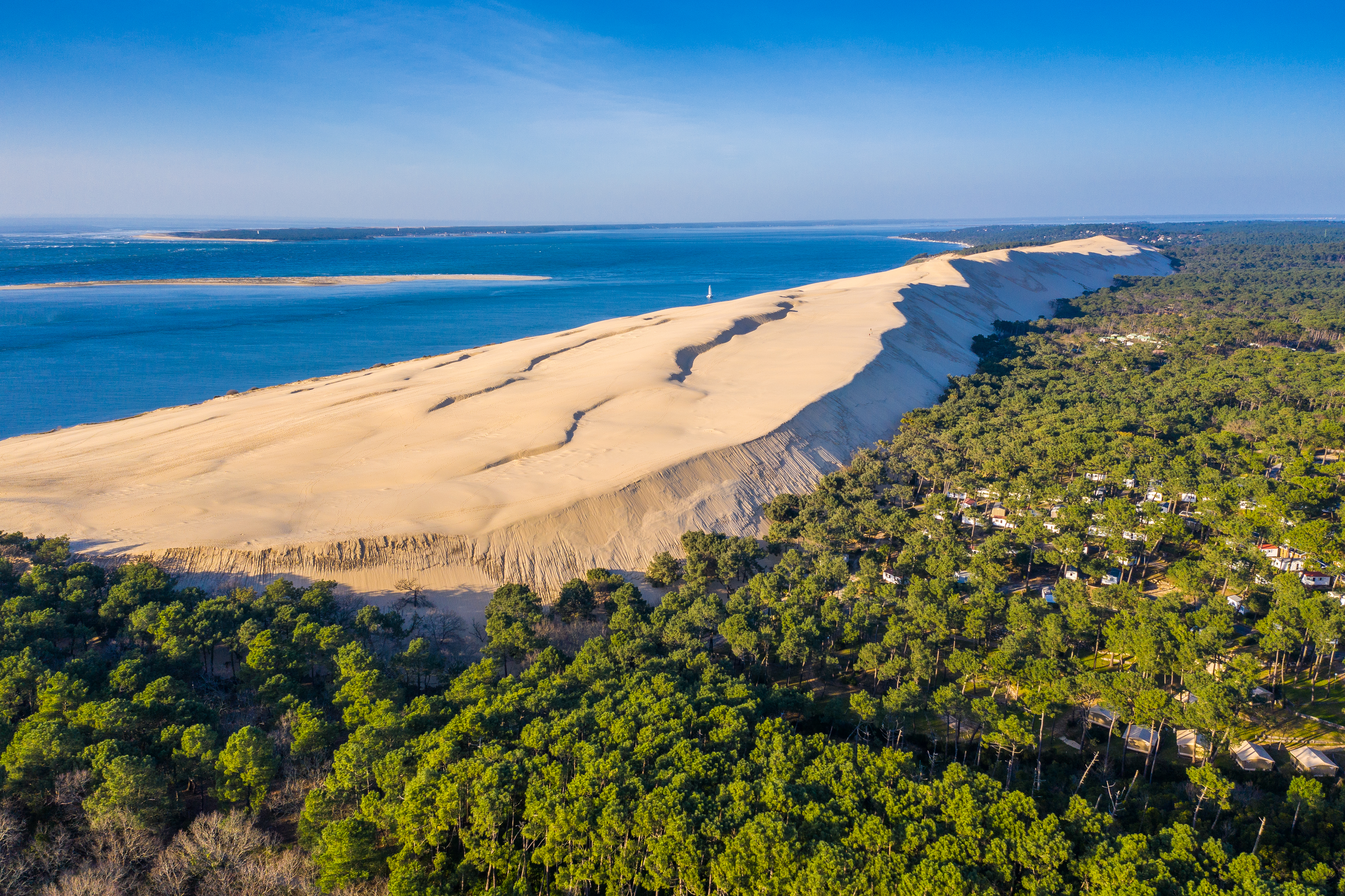 Luftfoto af den majestætiske Dune du Pilat nær Arcachon i Frankrig, omgivet af grøn fyrreskov og det blå Atlanterhav