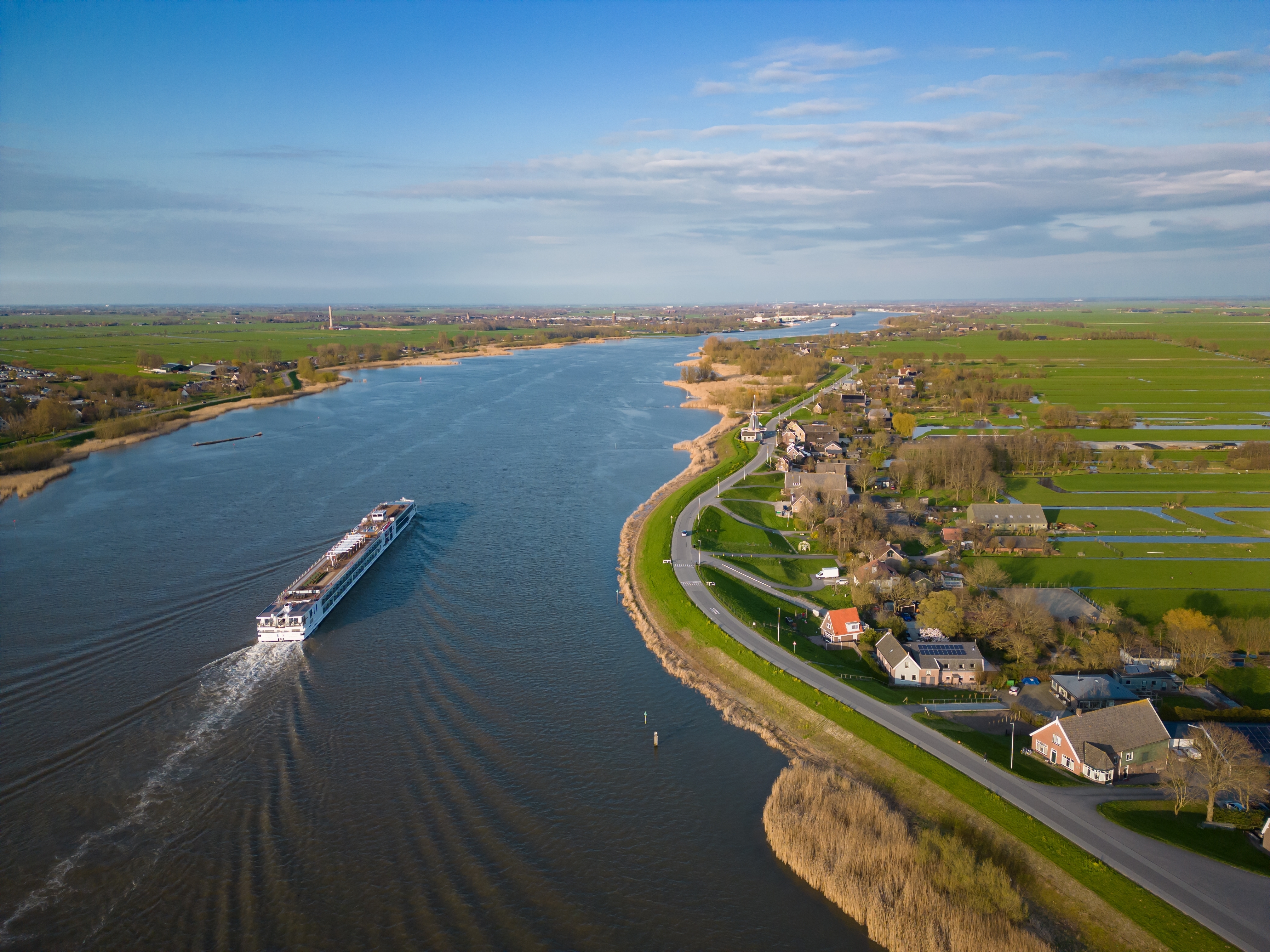 Dutch flodkrydstogt med skib forbi pittoresk landsby omgivet af grønne marker og vandområder