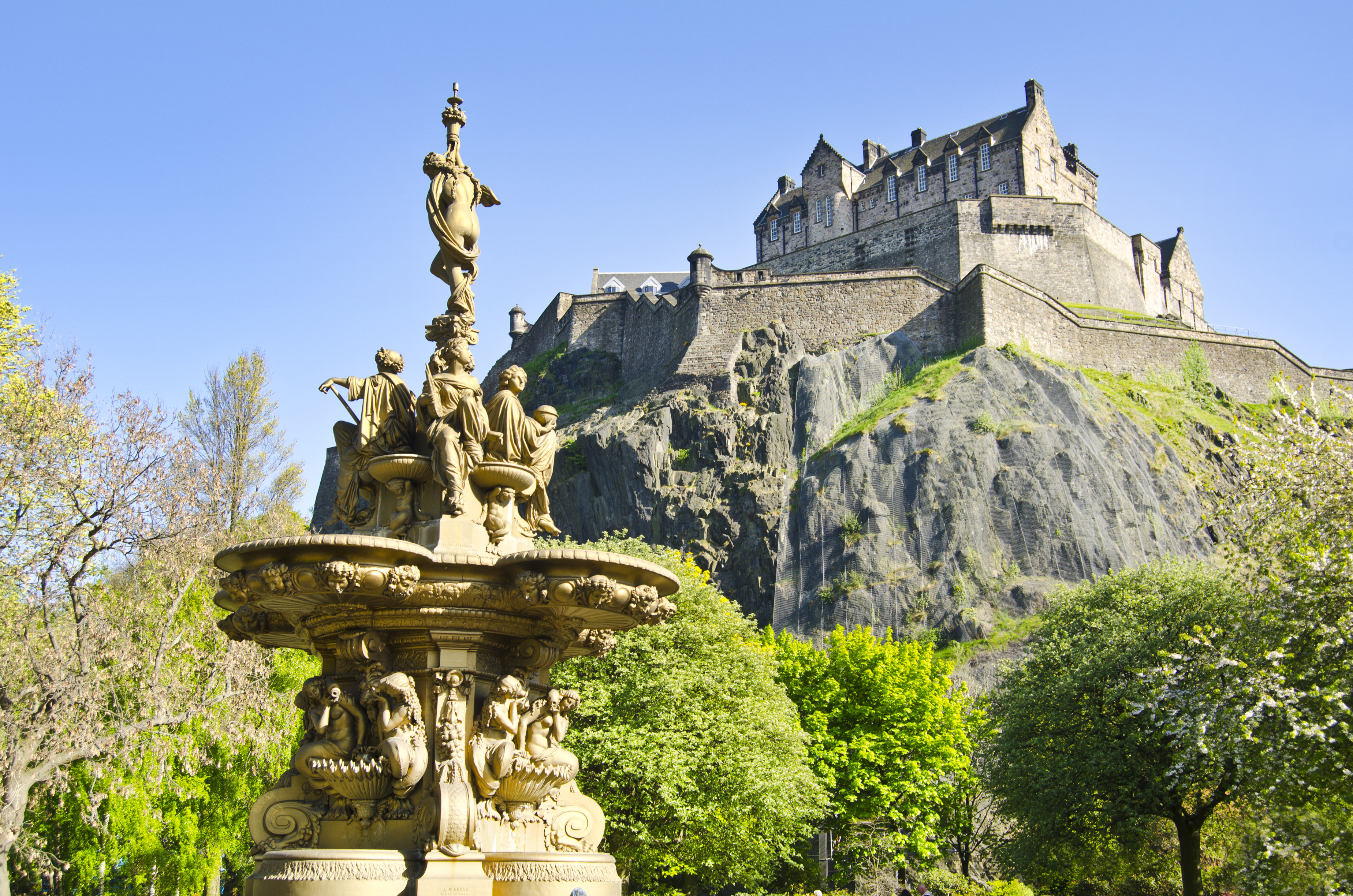 Den ikoniske Edinburgh Castle på klippeformation med den smukke Ross Fountain og grønne parkanlæg i forgrunden, Skotland