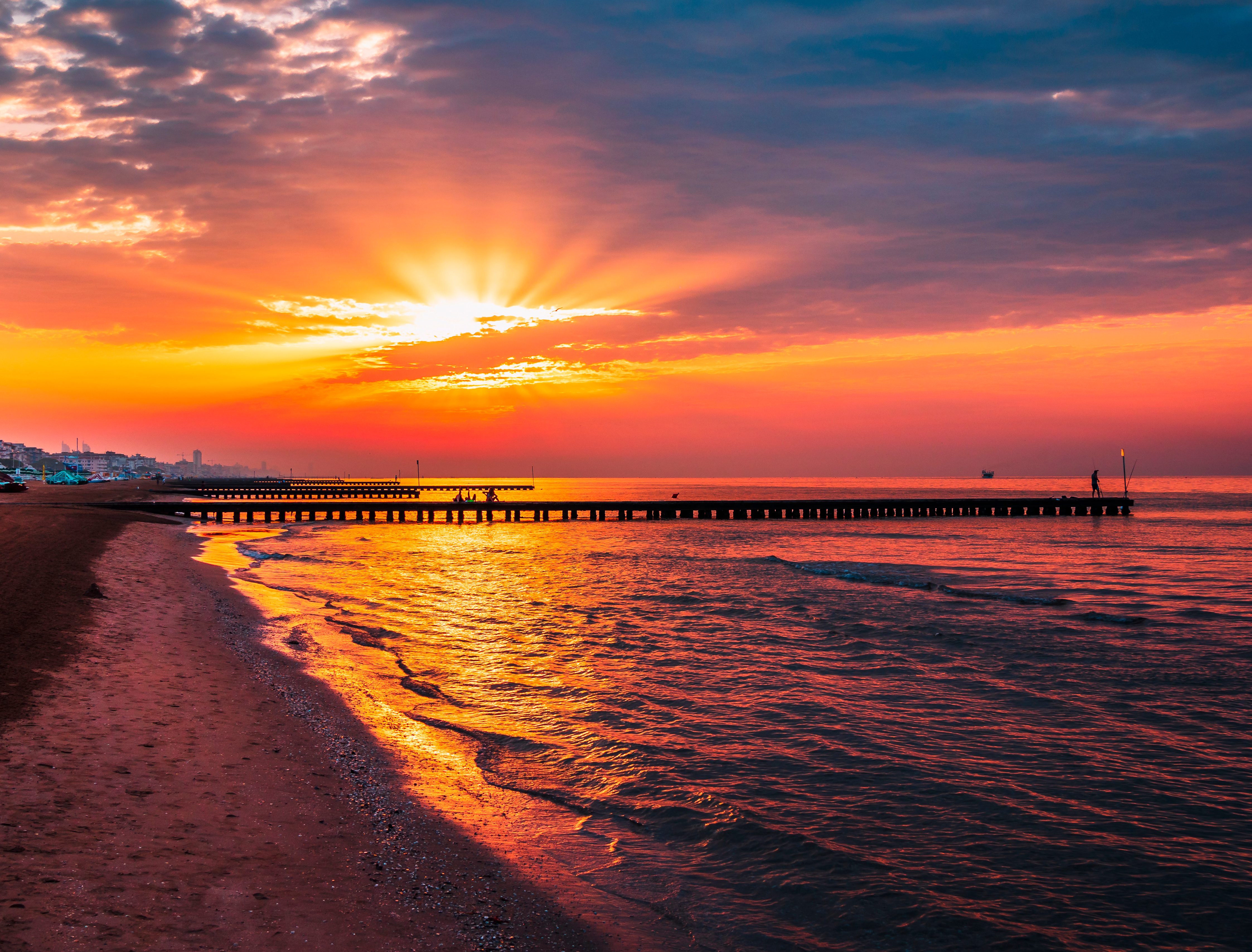 Eksotisk solnedgang ved havet med lang pier og spektakulære orange og røde farver reflekteret i det stille hav