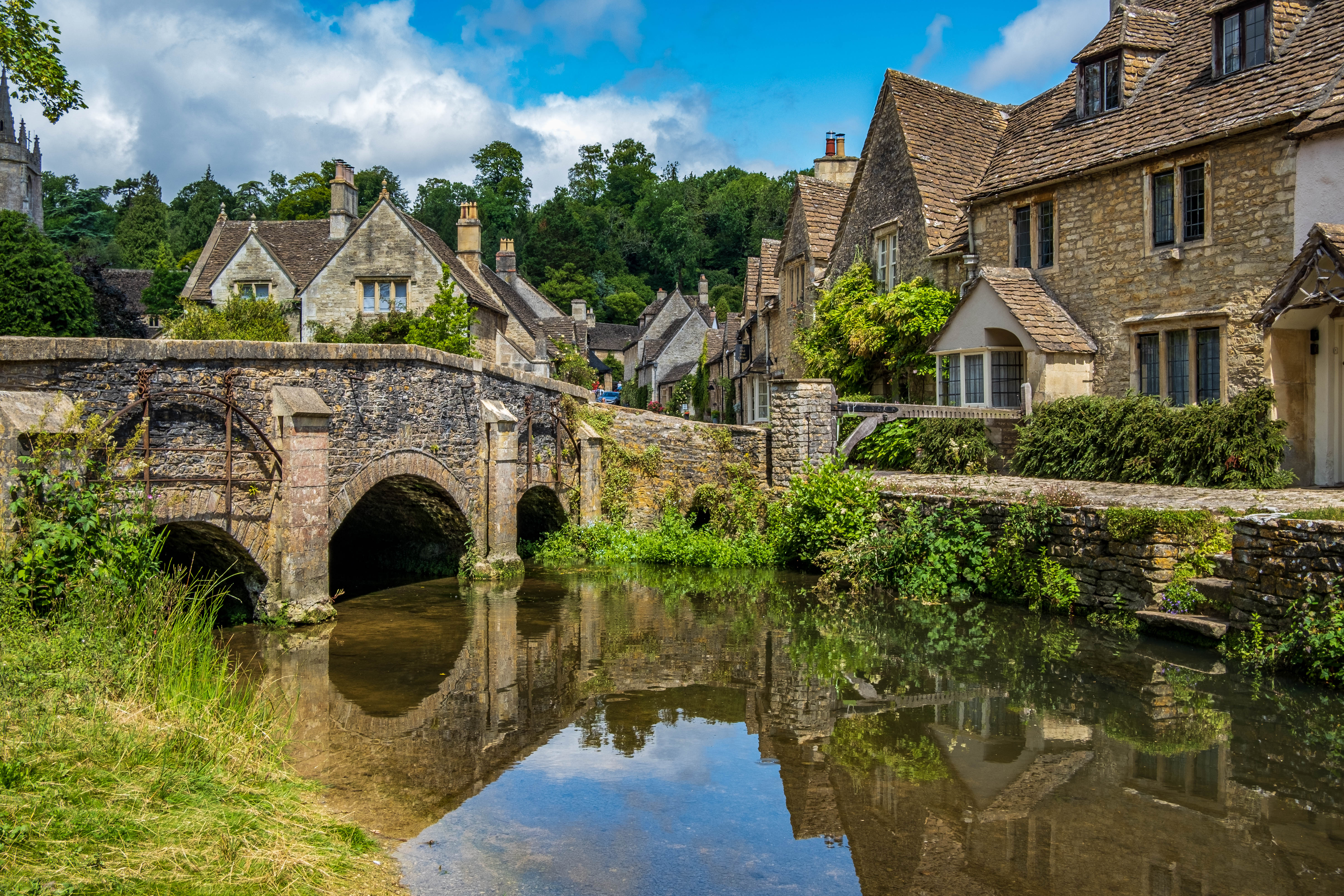 Idyllisk engelsk Cotswolds landsby med historisk stenbro og karakteristiske huse ved vandet