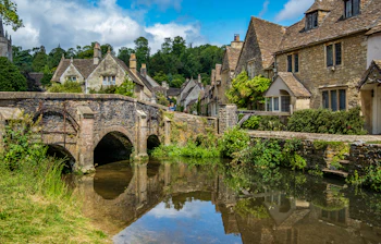 Idyllisk engelsk Cotswolds landsby med historisk stenbro og karakteristiske huse ved vandet