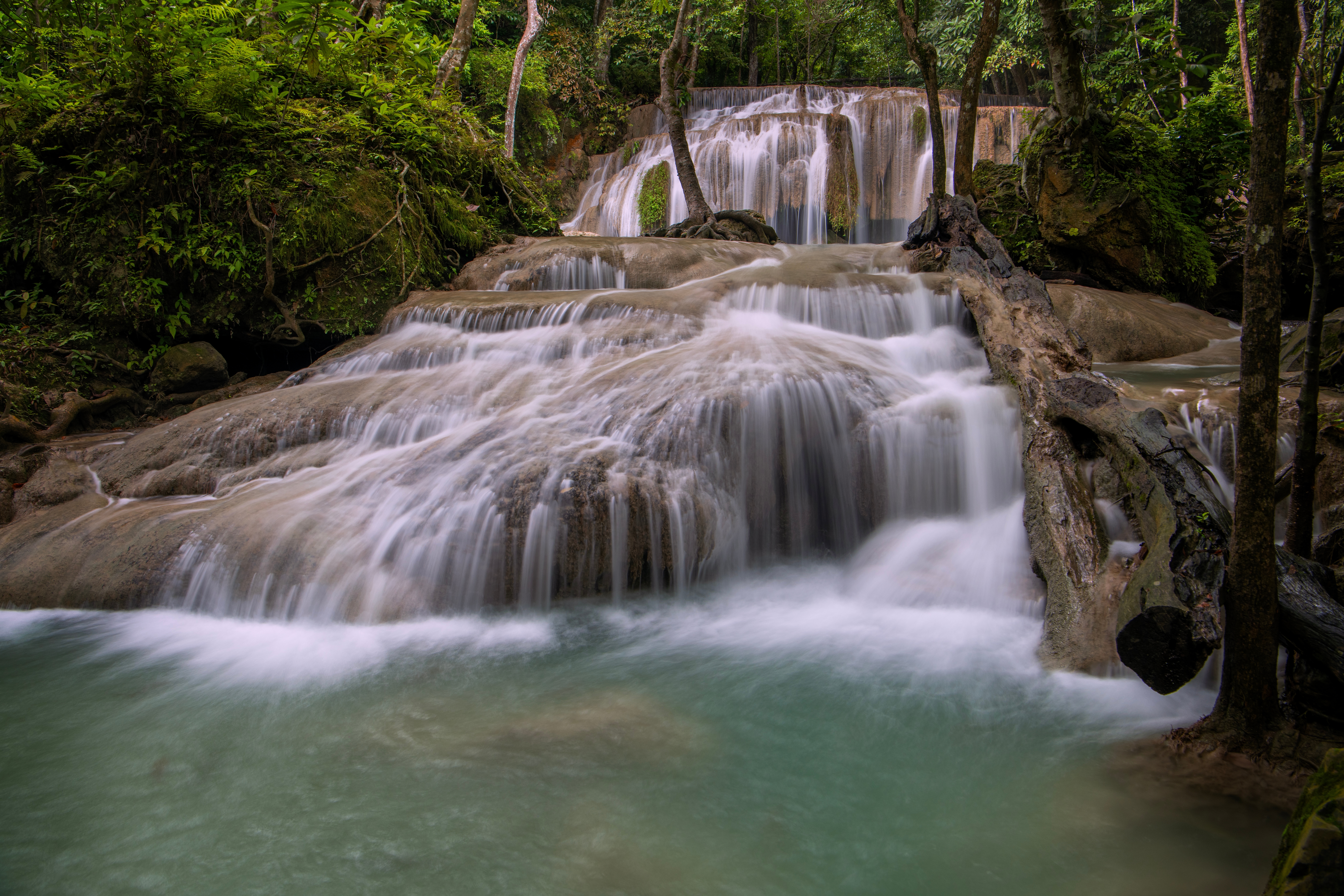 Eventyrligt Erawan vandfald i Kanchanaburi med turkisblåt vand der fosser ned over naturlige kalkstenstrin i tæt tropisk skov