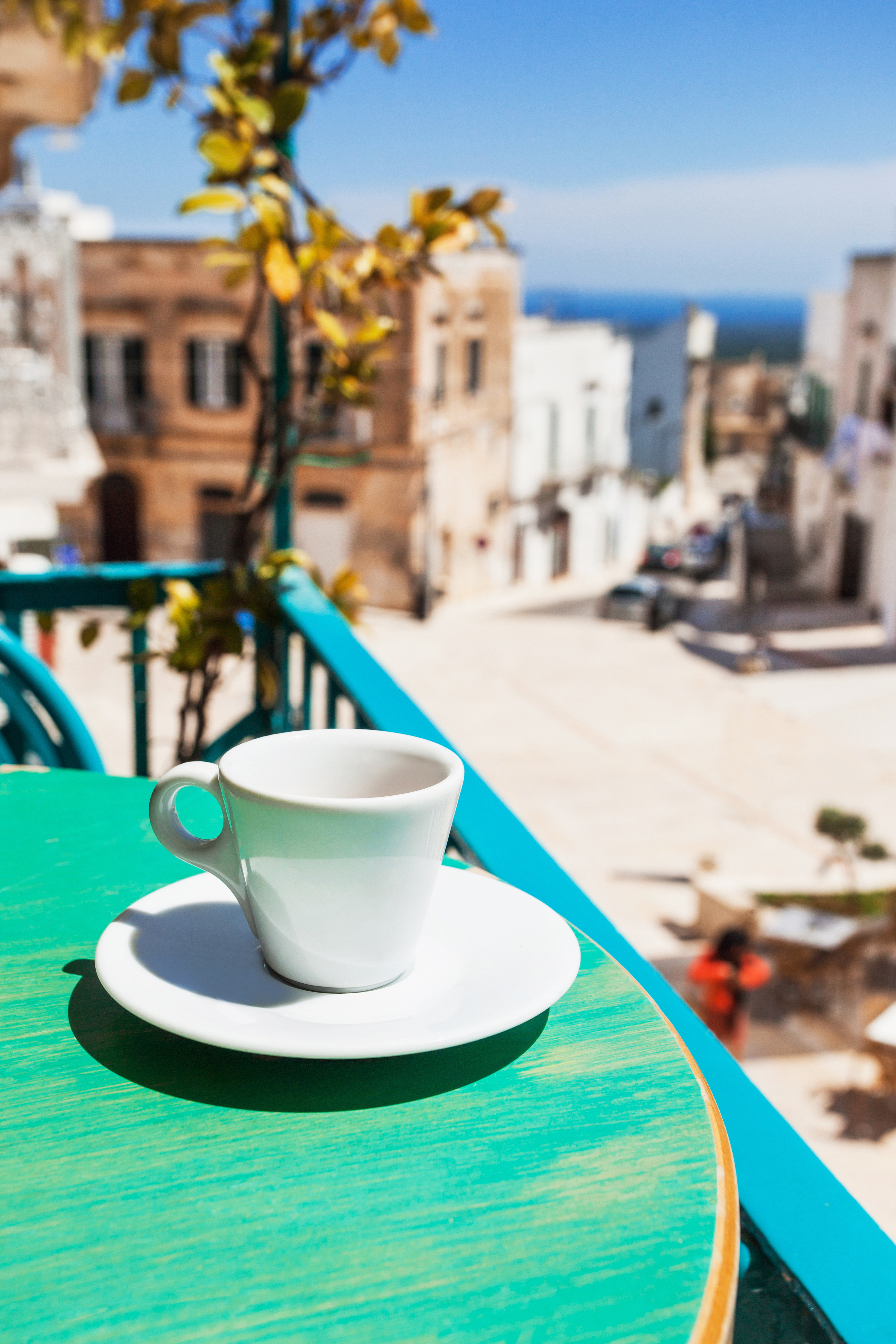Espressokop på turkis cafébord med udsigt over solbeskinnede gader i en syditalienisk kystby