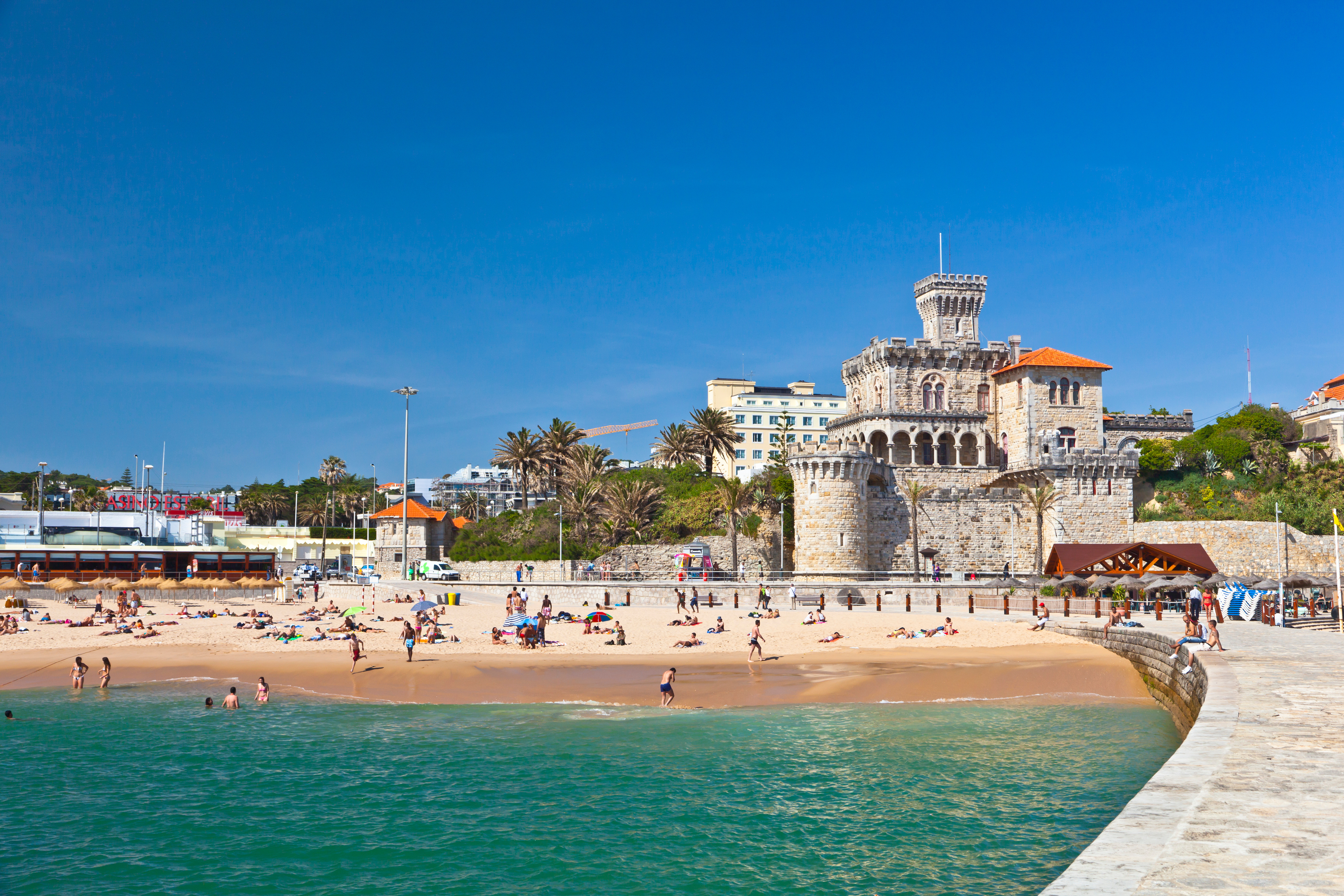 Den populære Estoril-strand på den portugisiske riviera med klart turkist vand og det karakteristiske Estoril Slot