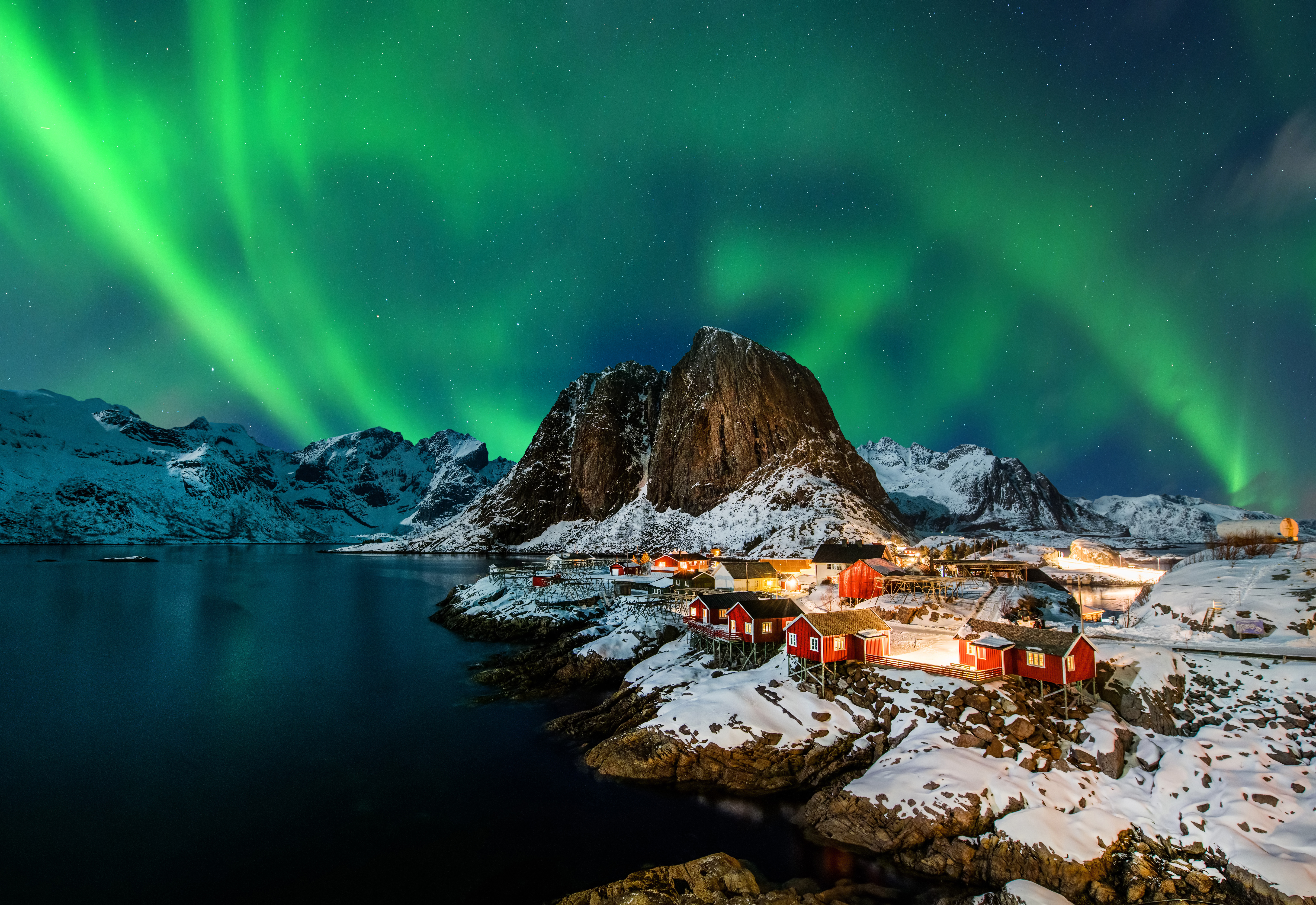Storslået nordlys lyser op over snedækkede bjerge og traditionelle fiskerhytter i Hamnøy, Lofoten - en unik norsk vinteroplevelse