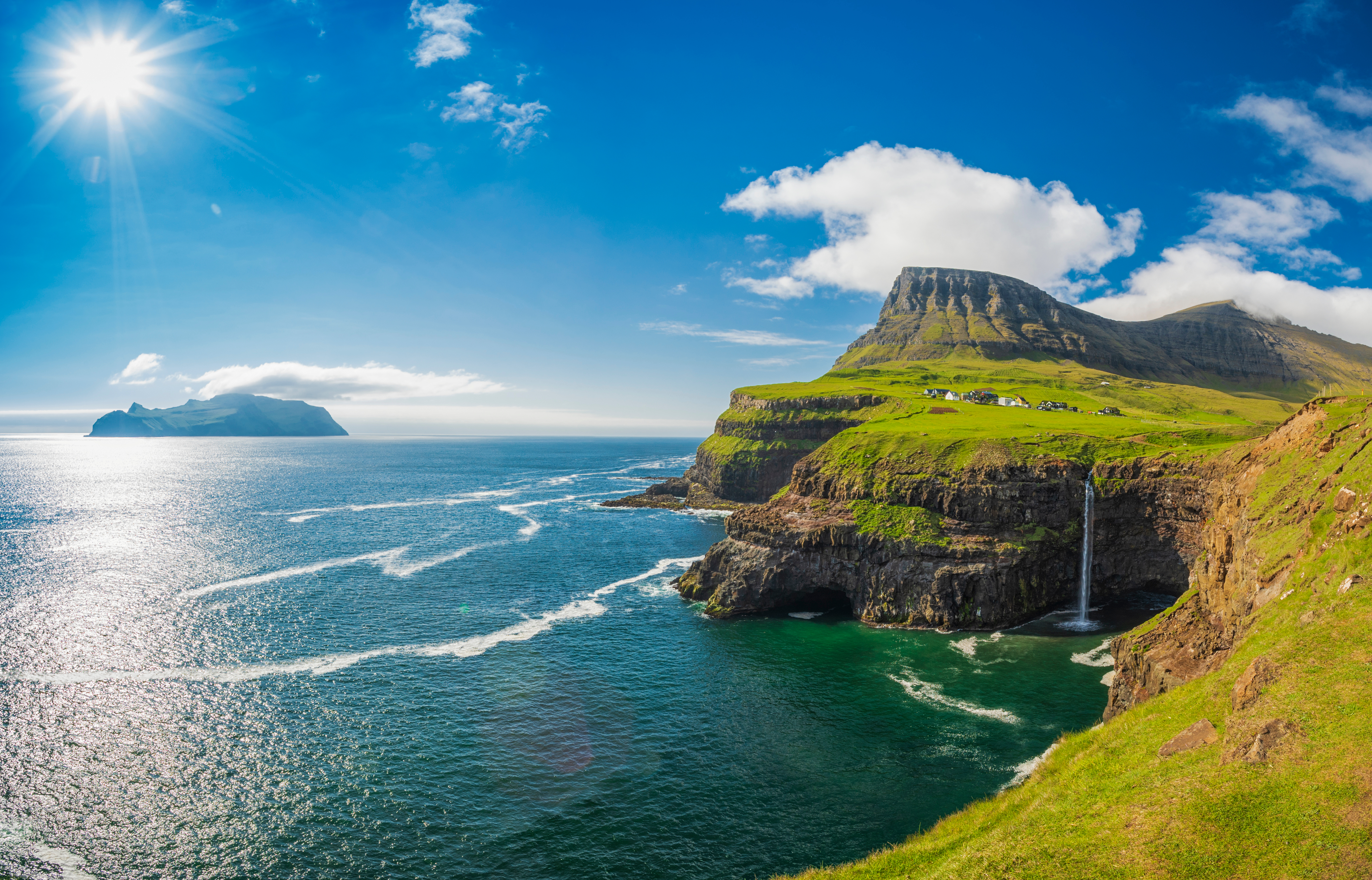 Majestætisk kystpanorama fra Færøerne med smaragdgrønt græs, stejle klipper og vandfald mod det turkise atlanterhav