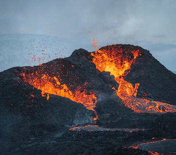 Naturfænomen på Island ved Fagradalsfjall vulkanen med kraftigt udbrud af glødende lava og magma fra krateret omgivet af sort vulkansk sten og snedækkede bjerge