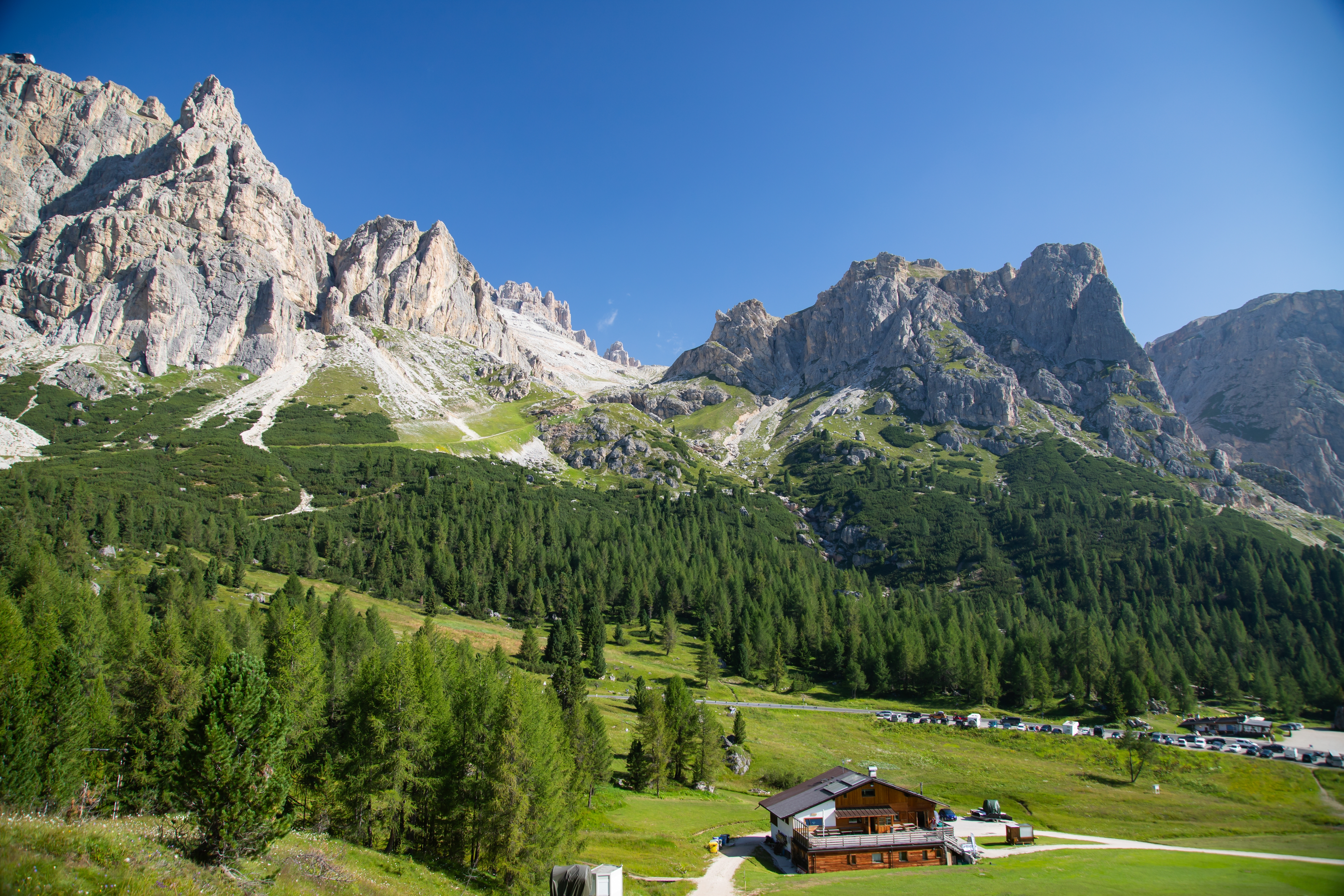 Panoramaudsigt over det alpine landskab ved Falzarego-passet i Dolomitterne med en traditionel rifugio, frodig grøn vegetation og markante bjergtinder i Norditalien