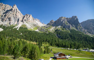 Panoramaudsigt over det alpine landskab ved Falzarego-passet i Dolomitterne med en traditionel rifugio, frodig grøn vegetation og markante bjergtinder i Norditalien