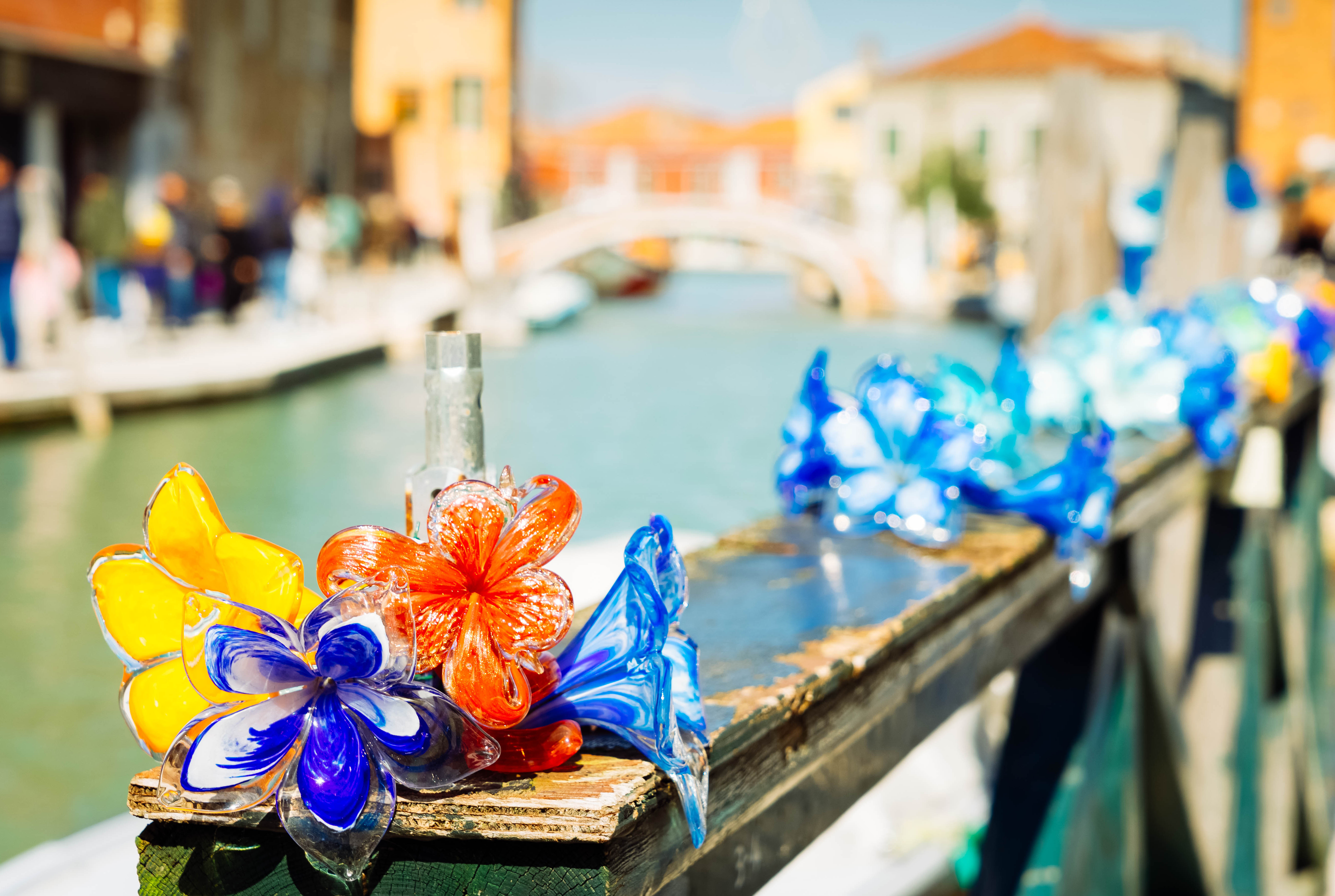 Karakteristiske håndlavede Murano glasblomster i blå, gule og orange nuancer opstillet ved en kanal på Murano øen i Venedig