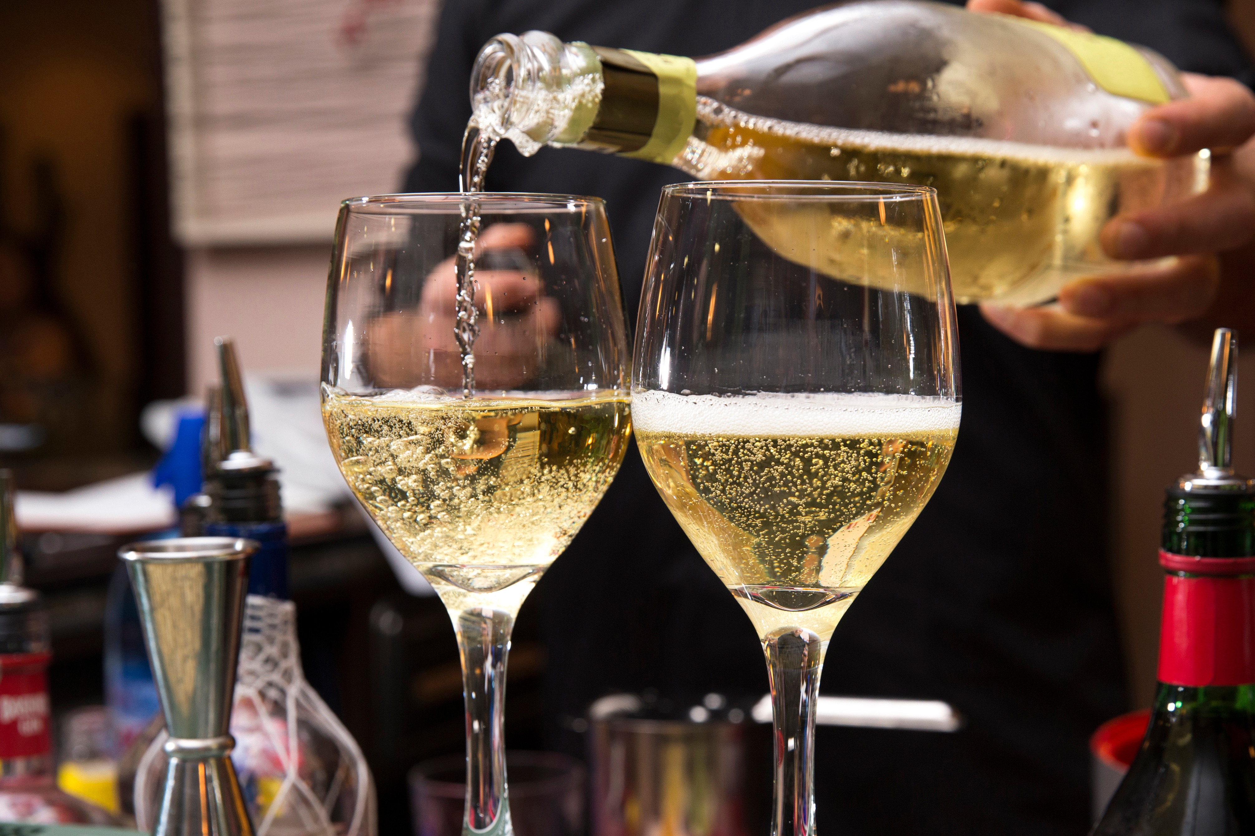 Bartender hælder frisk mousserende prosecco fra flaske i elegante vinglas ved festlig fejring på italiensk bar