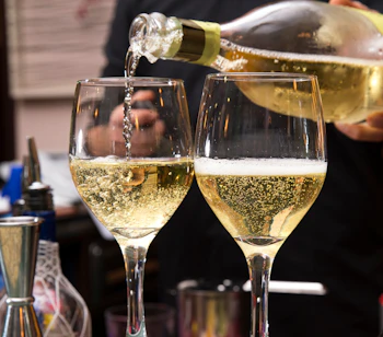 Bartender hælder frisk mousserende prosecco fra flaske i elegante vinglas ved festlig fejring på italiensk bar