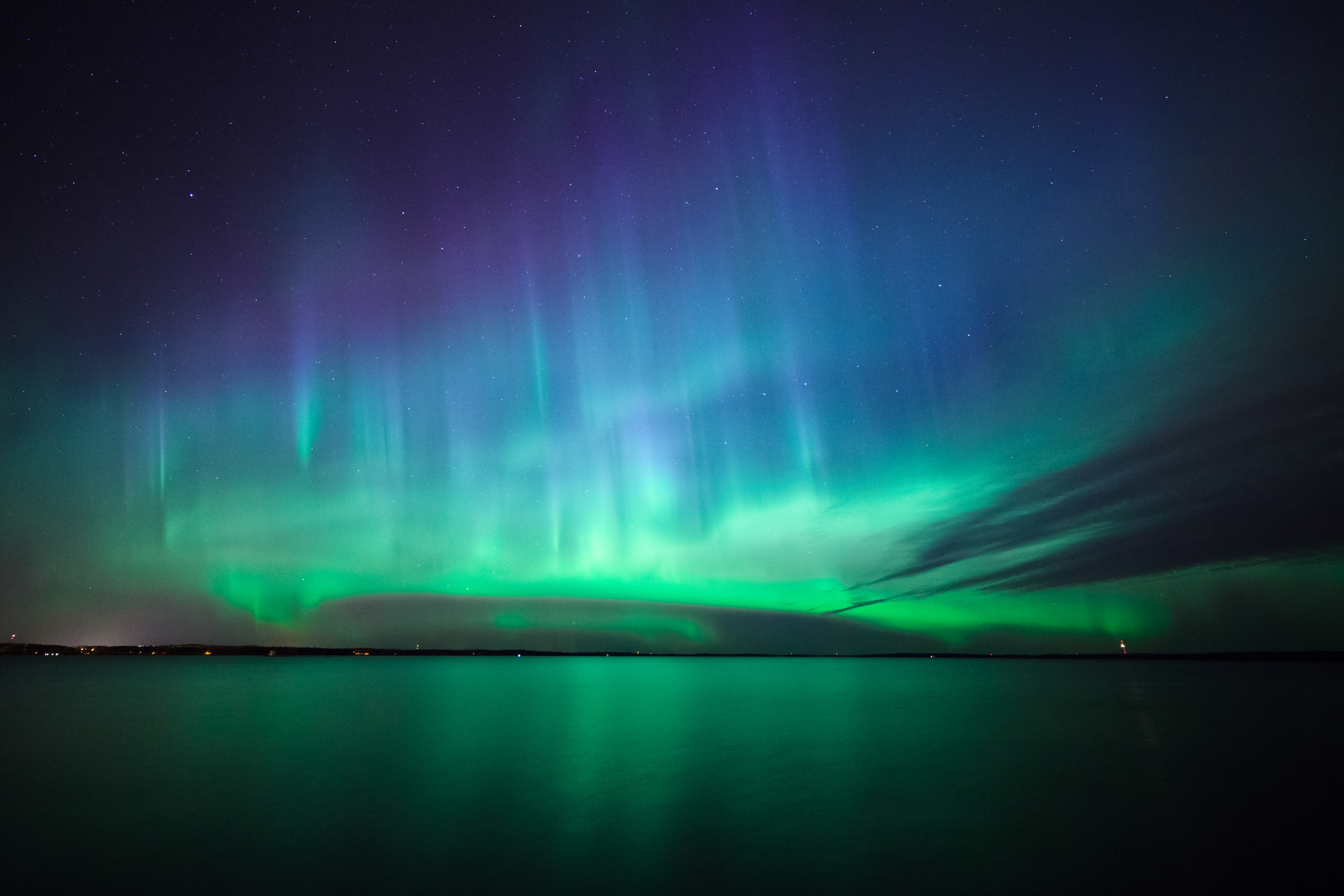 Utroligt nordlys i Finland med grøn og blå aurora der danser over stille sø med stjernerefleksioner