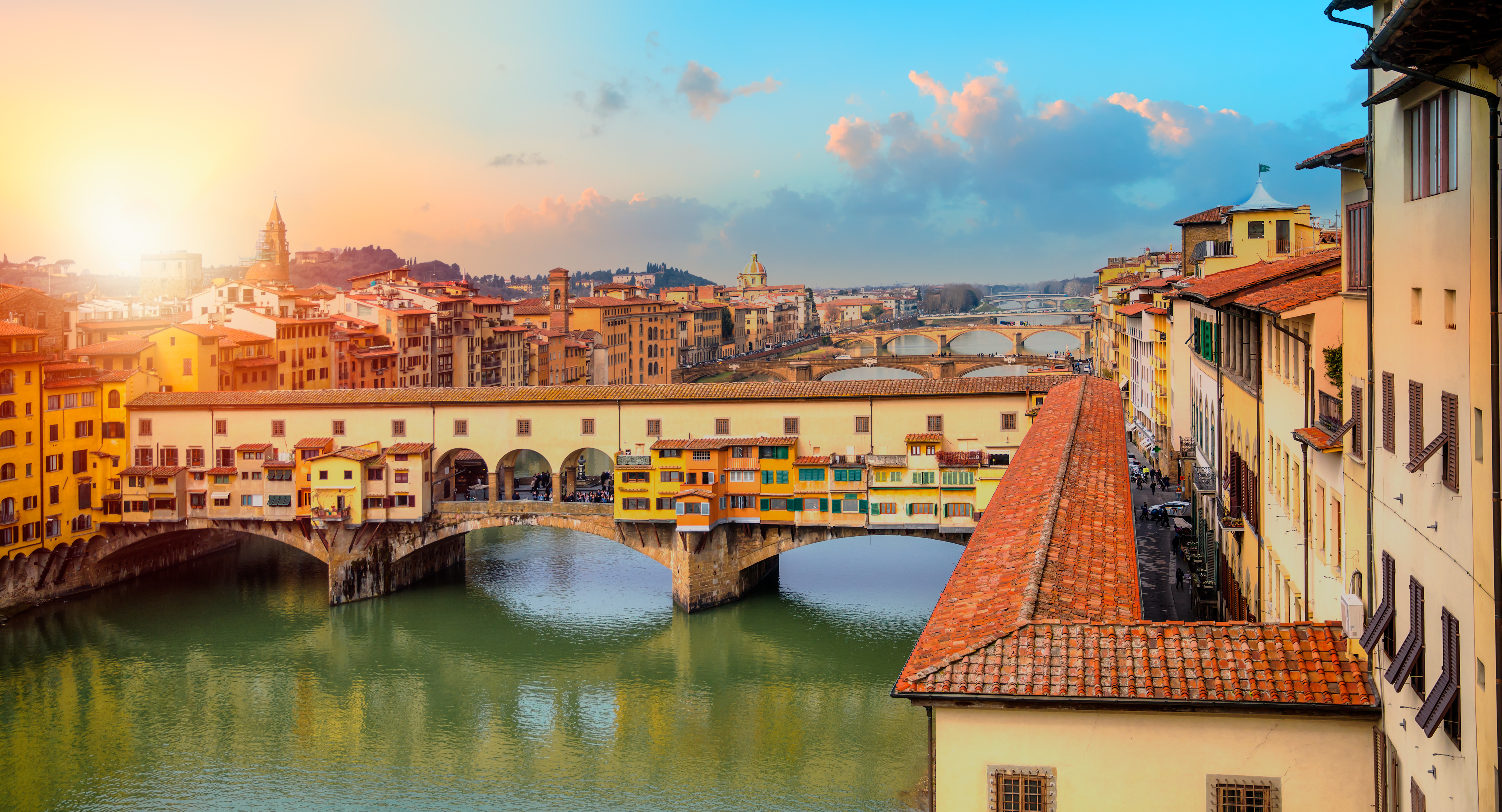 Udsigt til den berømte Ponte Vecchio bro i Firenze med sine karakteristiske butikker og gule facader over den skinnende Arno-flod