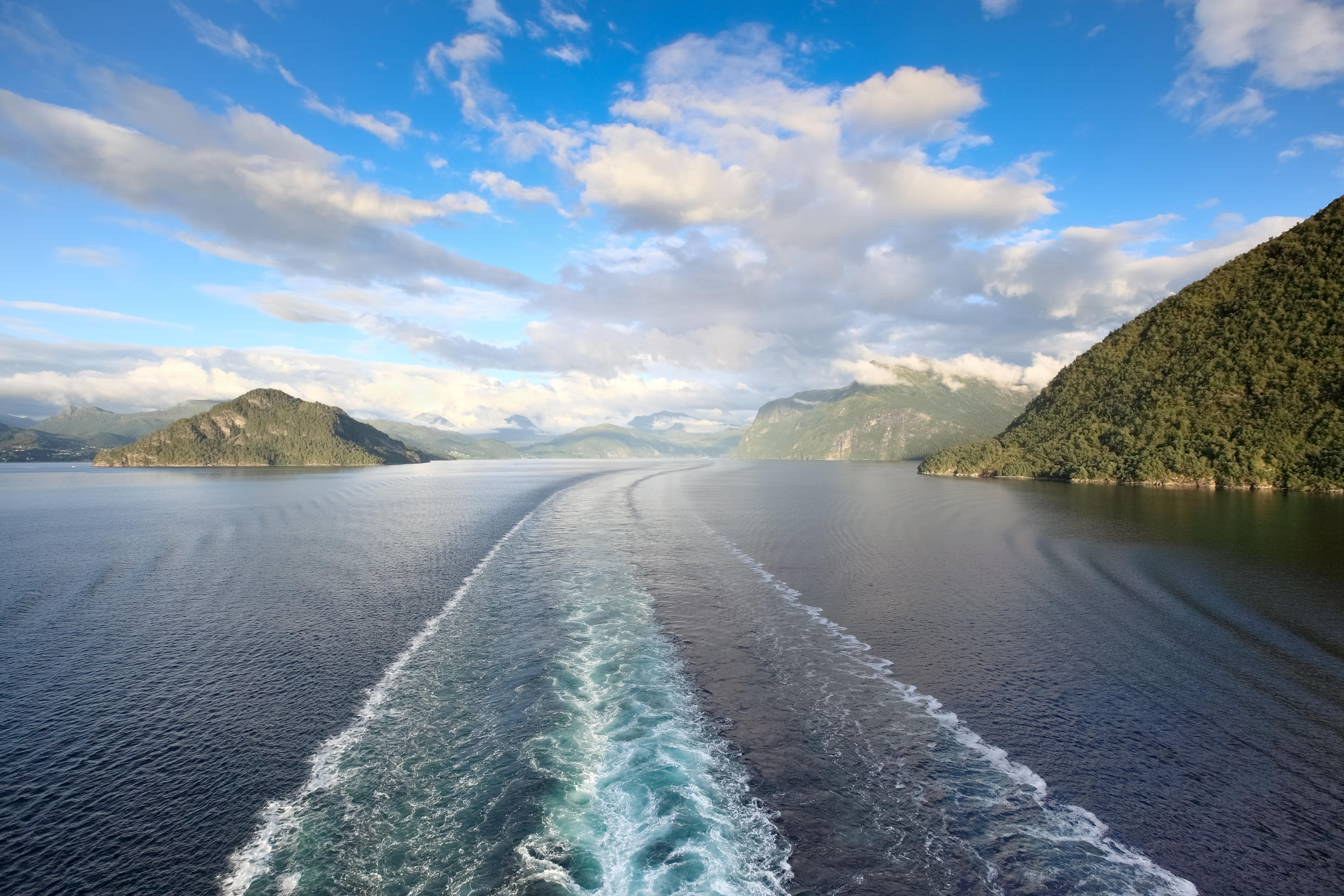 Fascinerende udsigt over Storfjorden fra krydstogtsskib i Norge, med spektakulære bjerge, grønne skråninger og det krystalklare fjordvand under den skandinaviske himmel