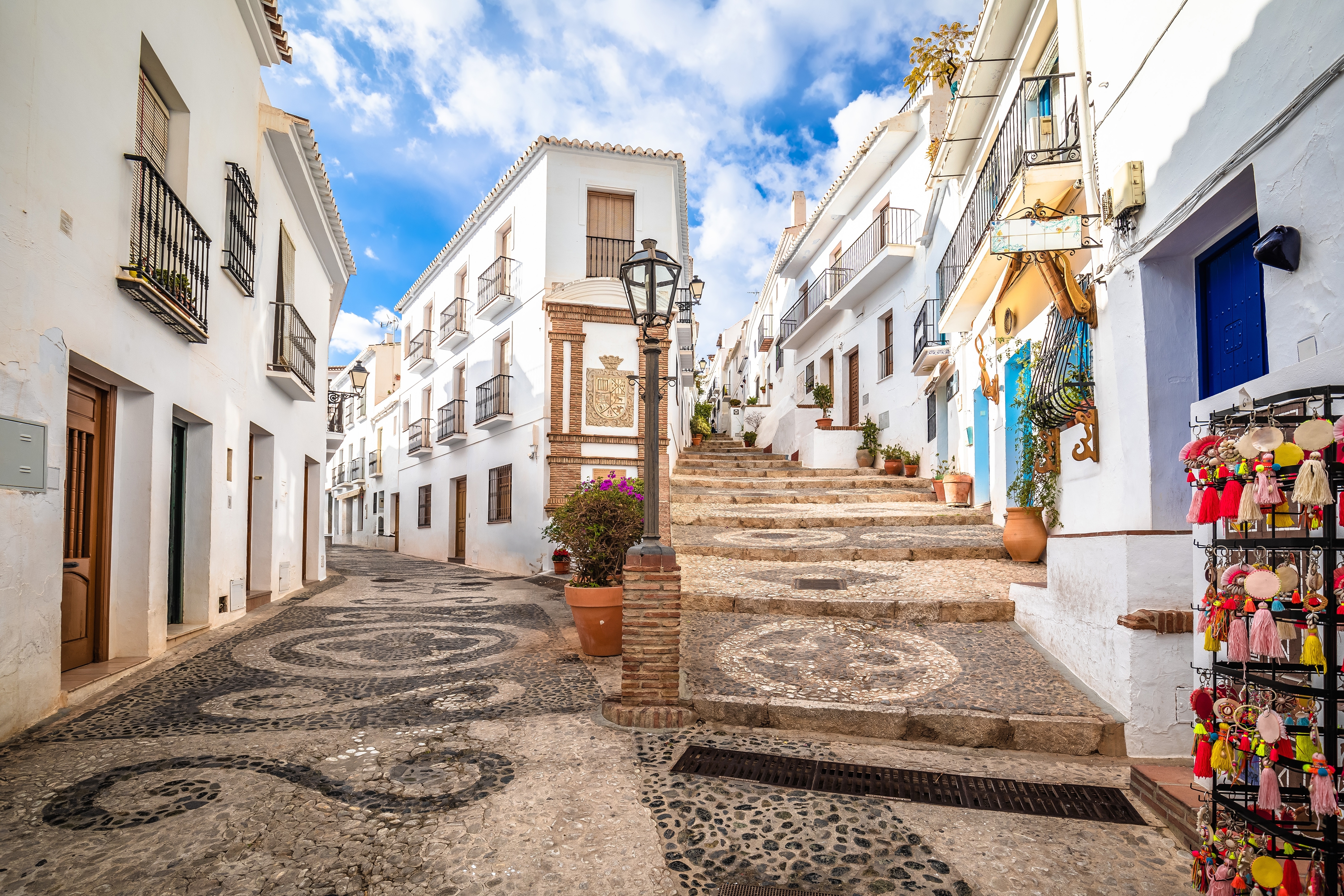 Malerisk gade i Frigiliana på Costa del Sol, Andalusien, med hvide huse, smukt mosaikbelagt stenbrolægning og farverig souvenirbutik
