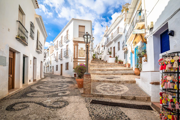 Malerisk gade i Frigiliana på Costa del Sol, Andalusien, med hvide huse, smukt mosaikbelagt stenbrolægning og farverig souvenirbutik