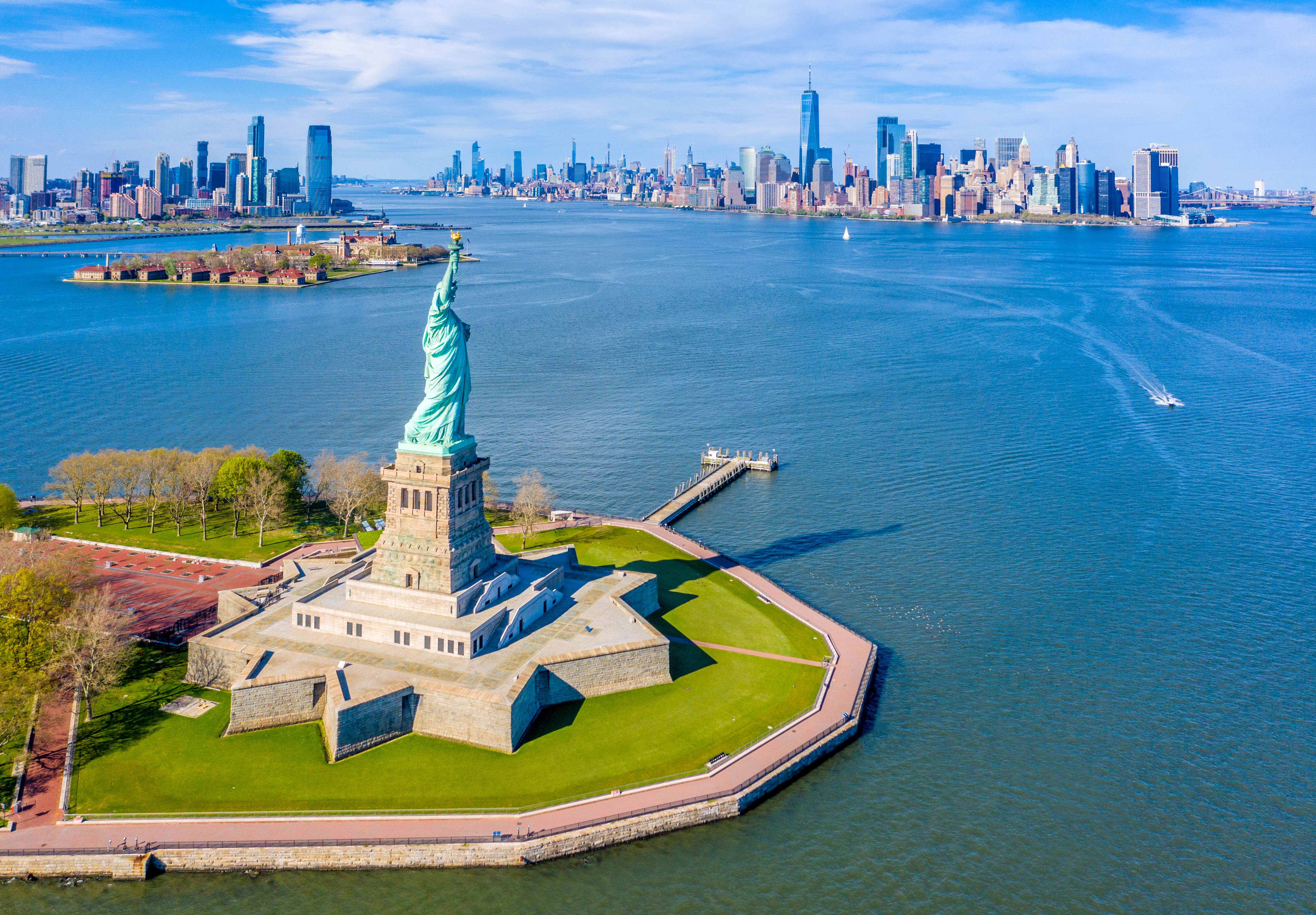 Flot luftperspektiv af Frihedsgudinden på Liberty Island med Ellis Island og Lower Manhattan skyline i baggrunden