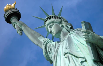 Majestætisk Frihedsgudinde i New York City med gyldent fakkel og karakteristisk krone mod blå himmel