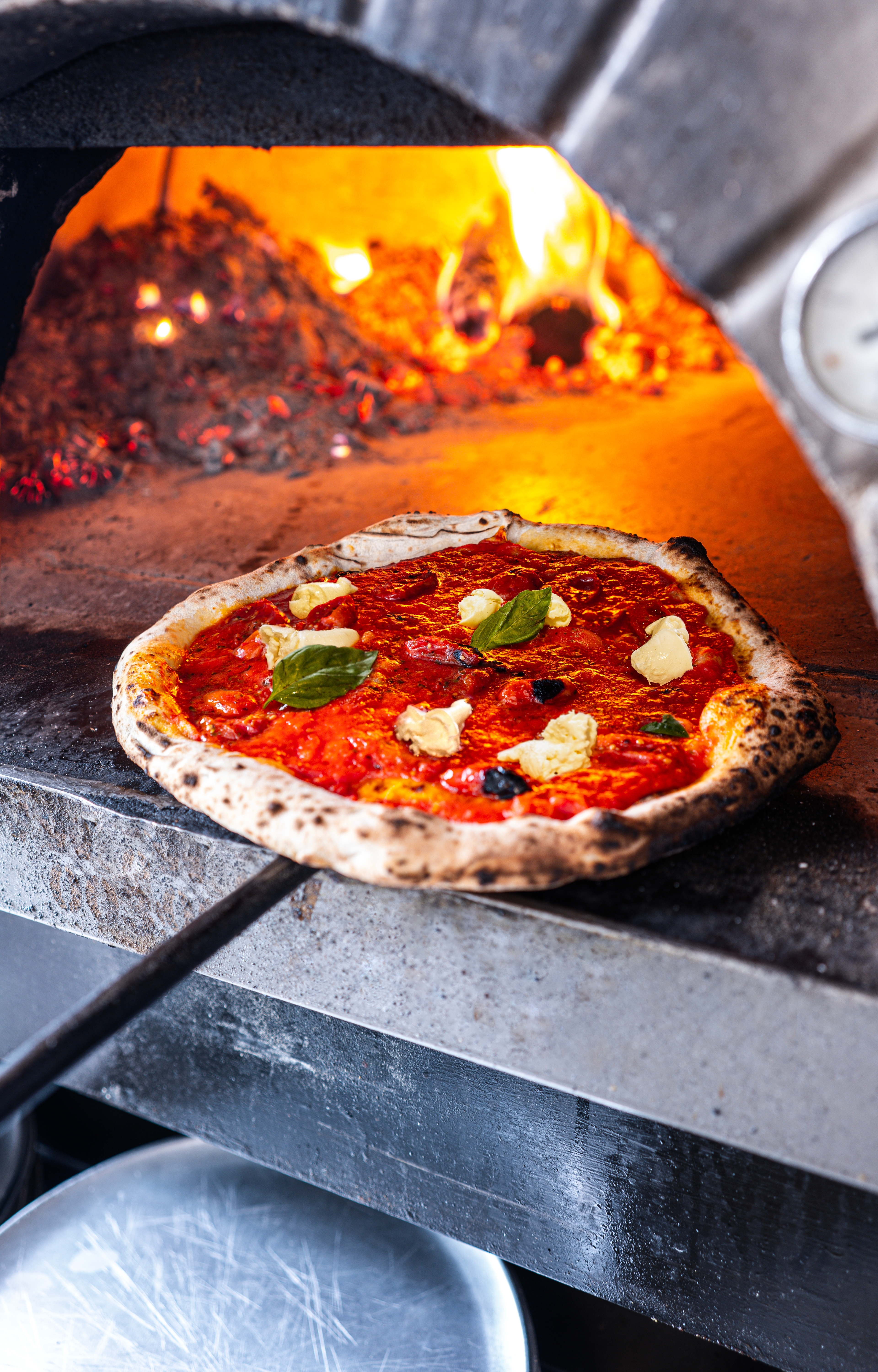 Friskbagt Margherita pizza tages ud af en glødende brændeovn i en traditionel italiensk pizzeria i Napoli