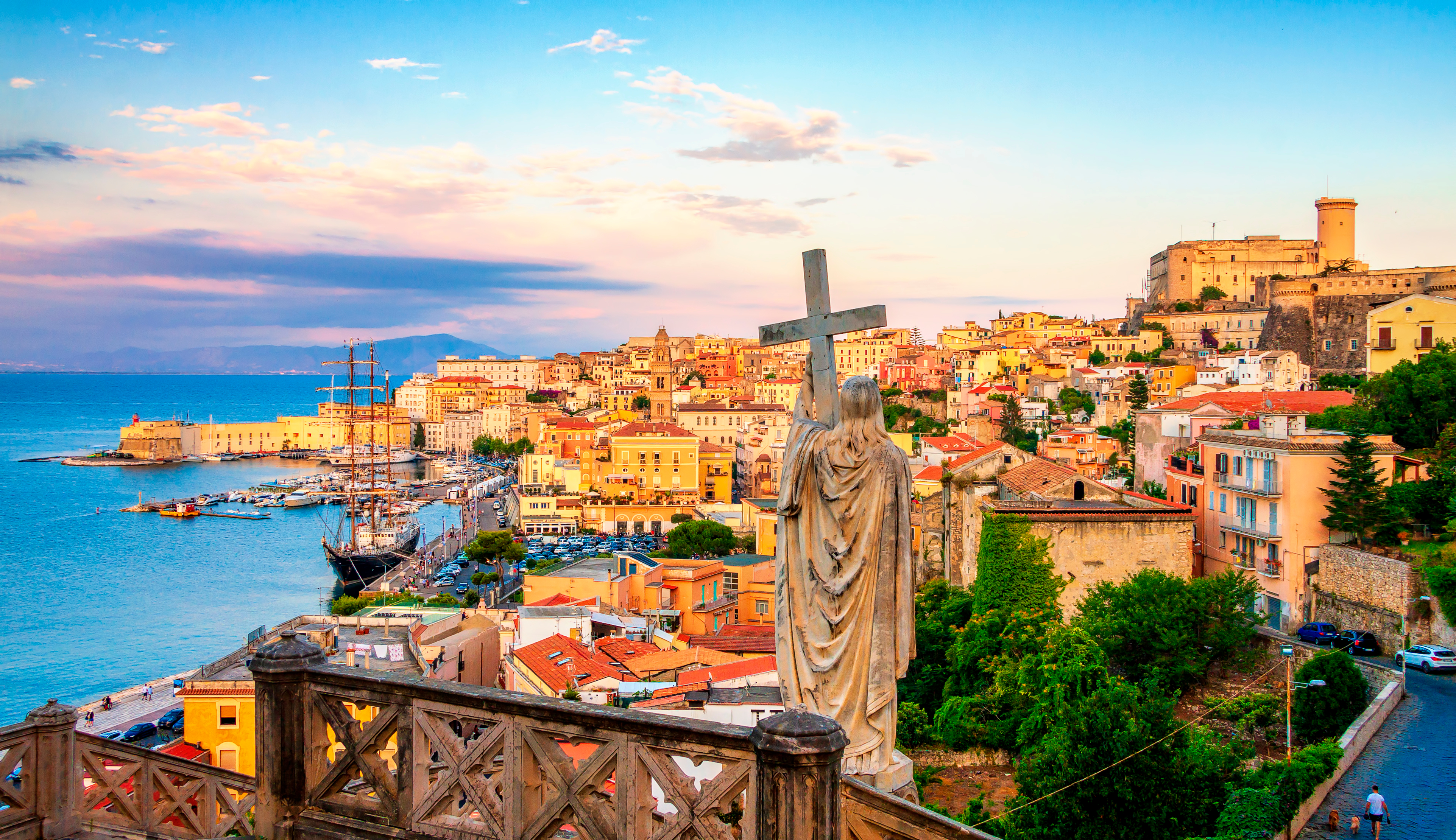 Panoramaudsigt over den historiske by Gaeta i Lazio, Italien, med Sankt Francesco-statue, farverige bygninger og havn ved solnedgang