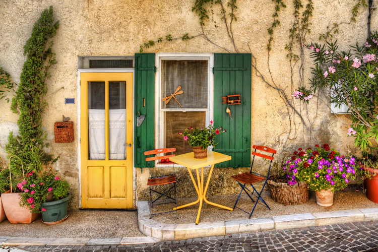 Gamle bydel café med gul bistrobord, farverige skodder og blomsterkrukker på pittoresk terrasse