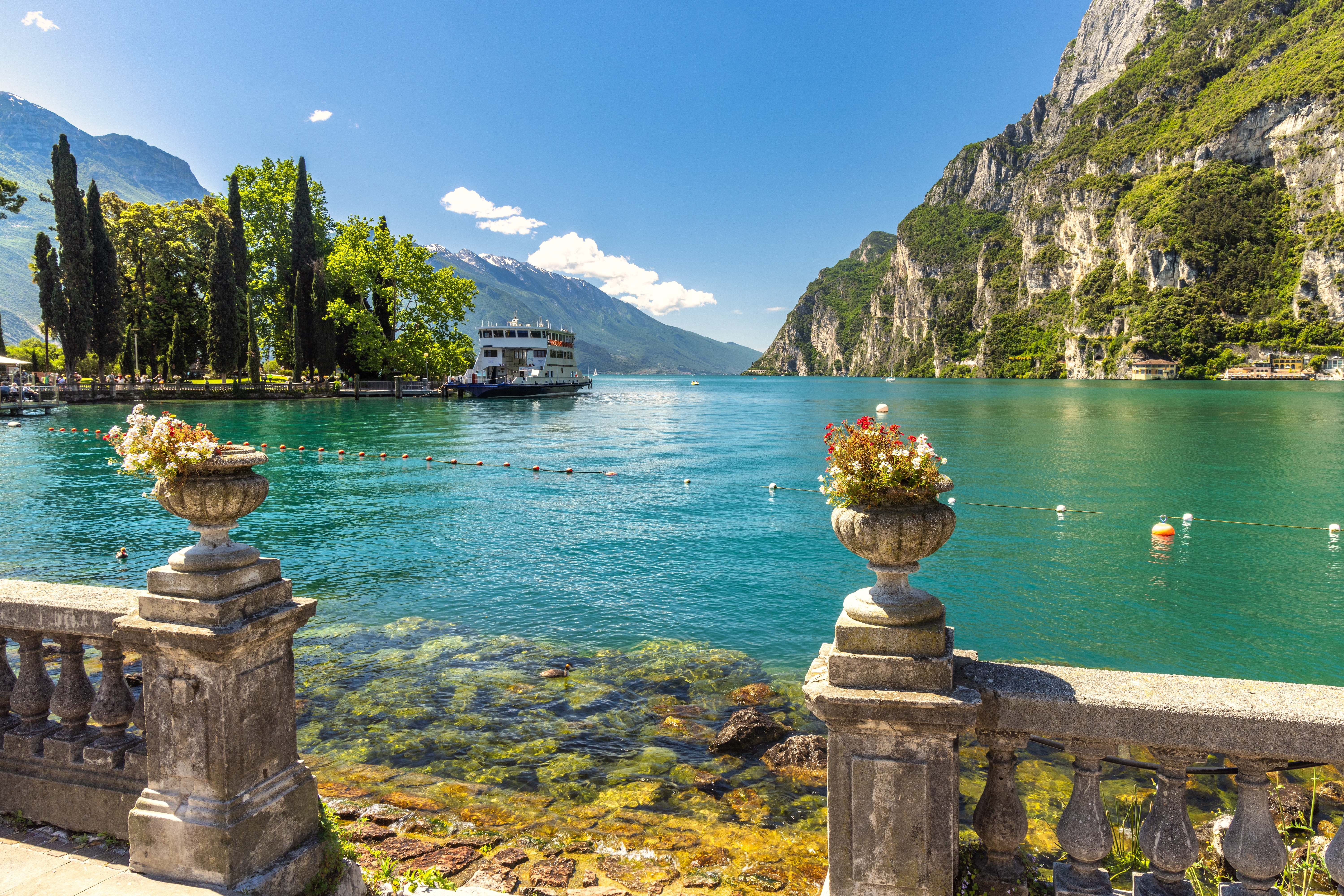 Gardasøen Italien med turistfærge og bjergkæder set fra elegant terrasse med klassiske blomsterurner