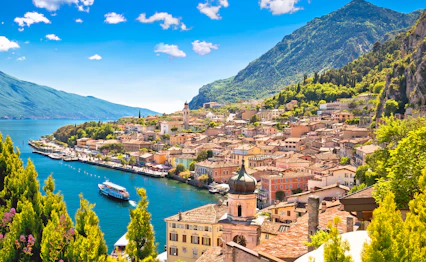 Malerisk udsigt over Limone sul Garda med farverige huse, kirkespir og en lystbåd på det turkisblå Gardasø med bjerge i baggrunden