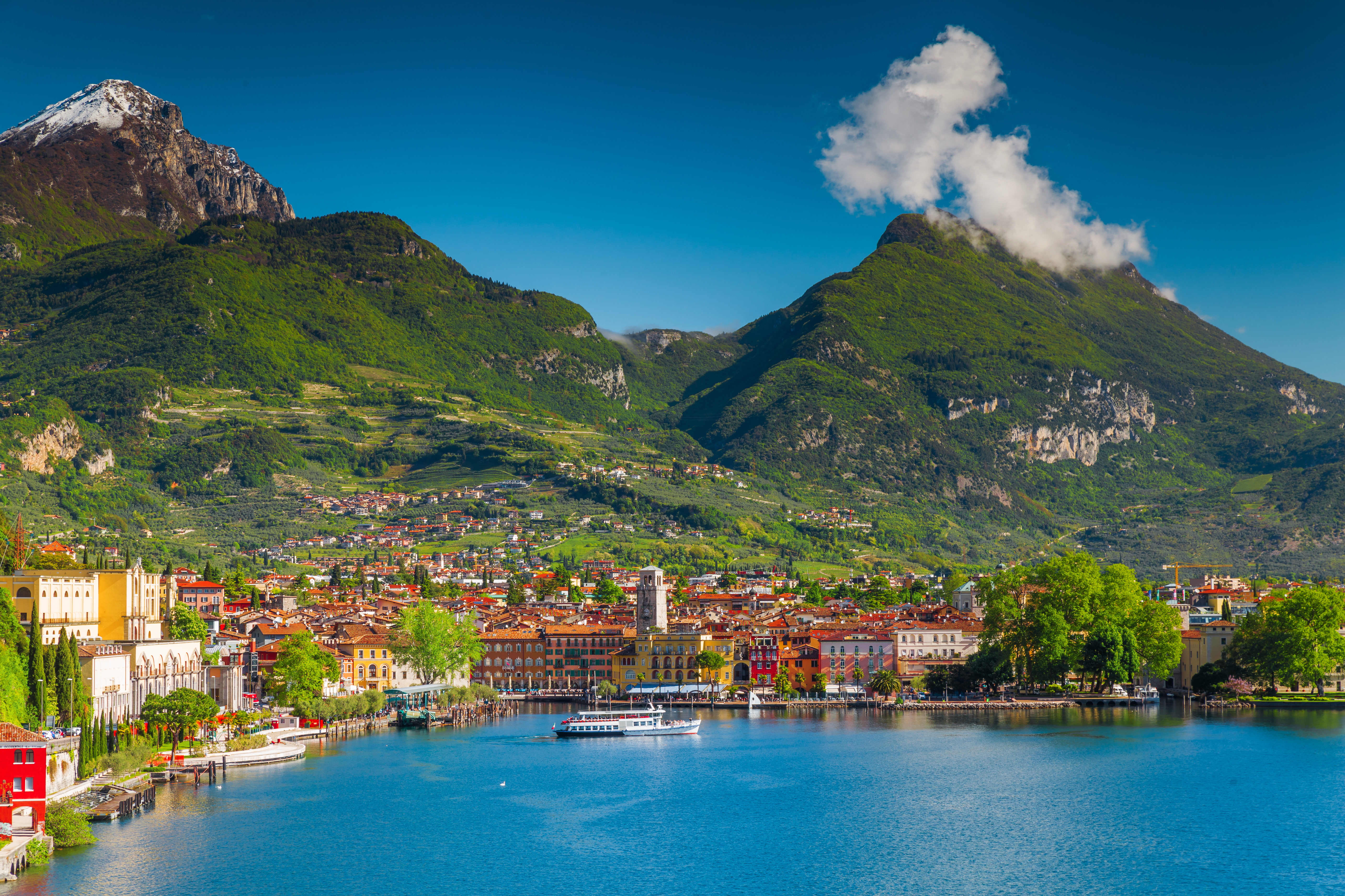 Idyllisk udsigt over Riva del Garda ved Gardasøen med farverige italienske bygninger, blåt vand og grønne alpebjerge i baggrunden