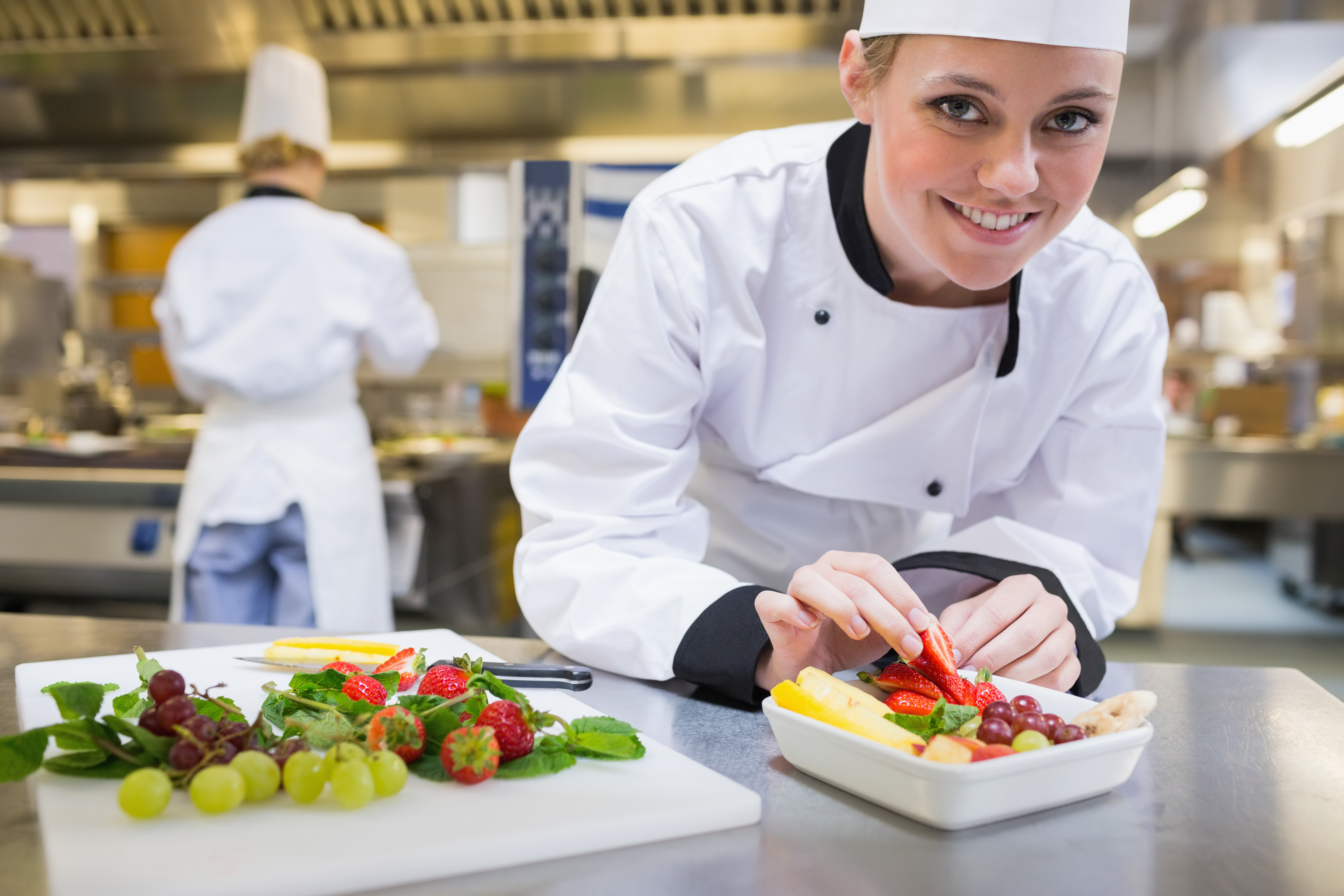 Smilende professionel kok tilføjer et jordbær til en farverig frugtsalat - repræsenterer de kulinariske oplevelser på Nille Rejsers rejsedestinationer