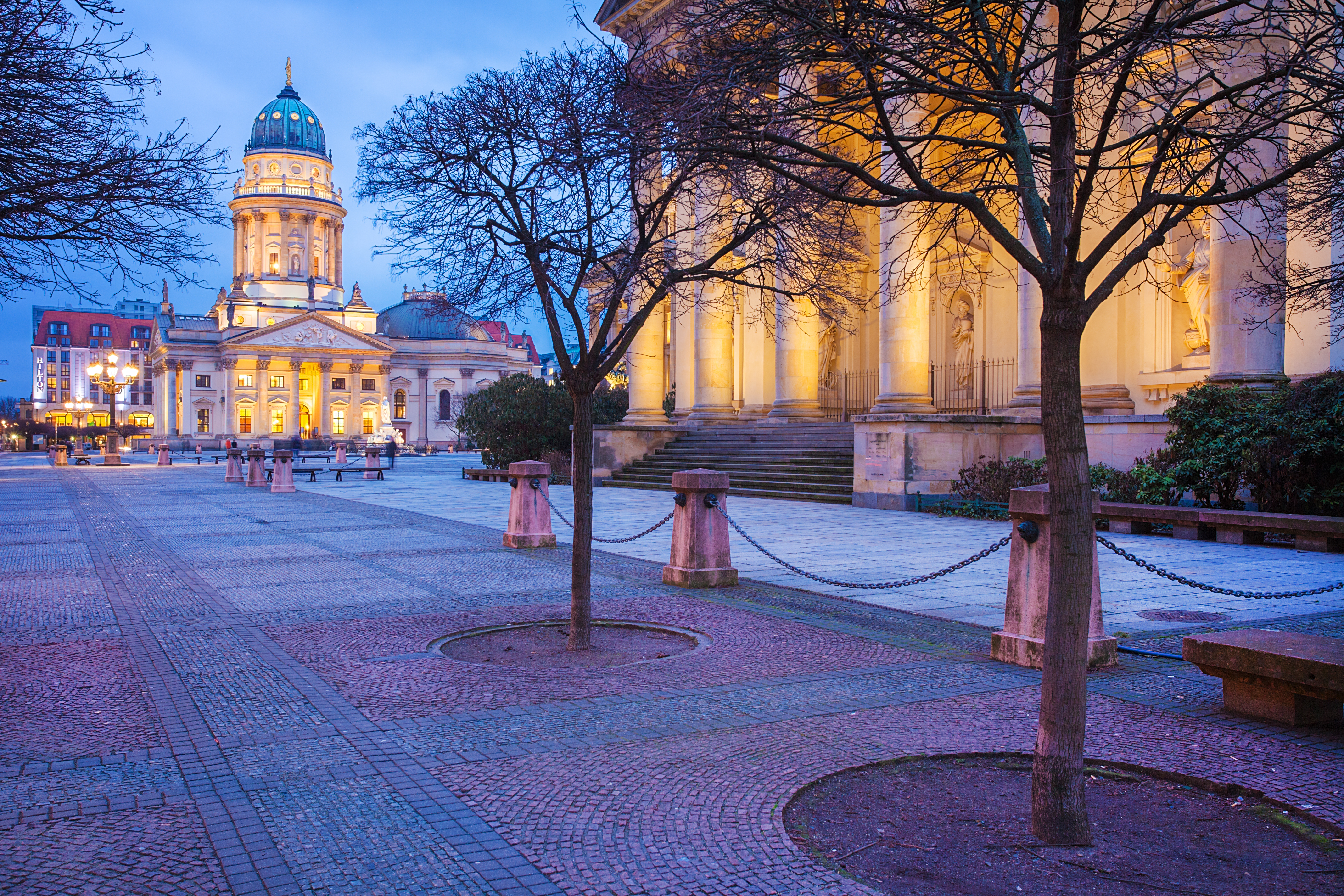 Historisk Gendarmenmarkt plads i Berlin ved tusmørke med den pragtfulde Tyske Dom oplyst om aftenen og klassiske søjler på den nærliggende bygning