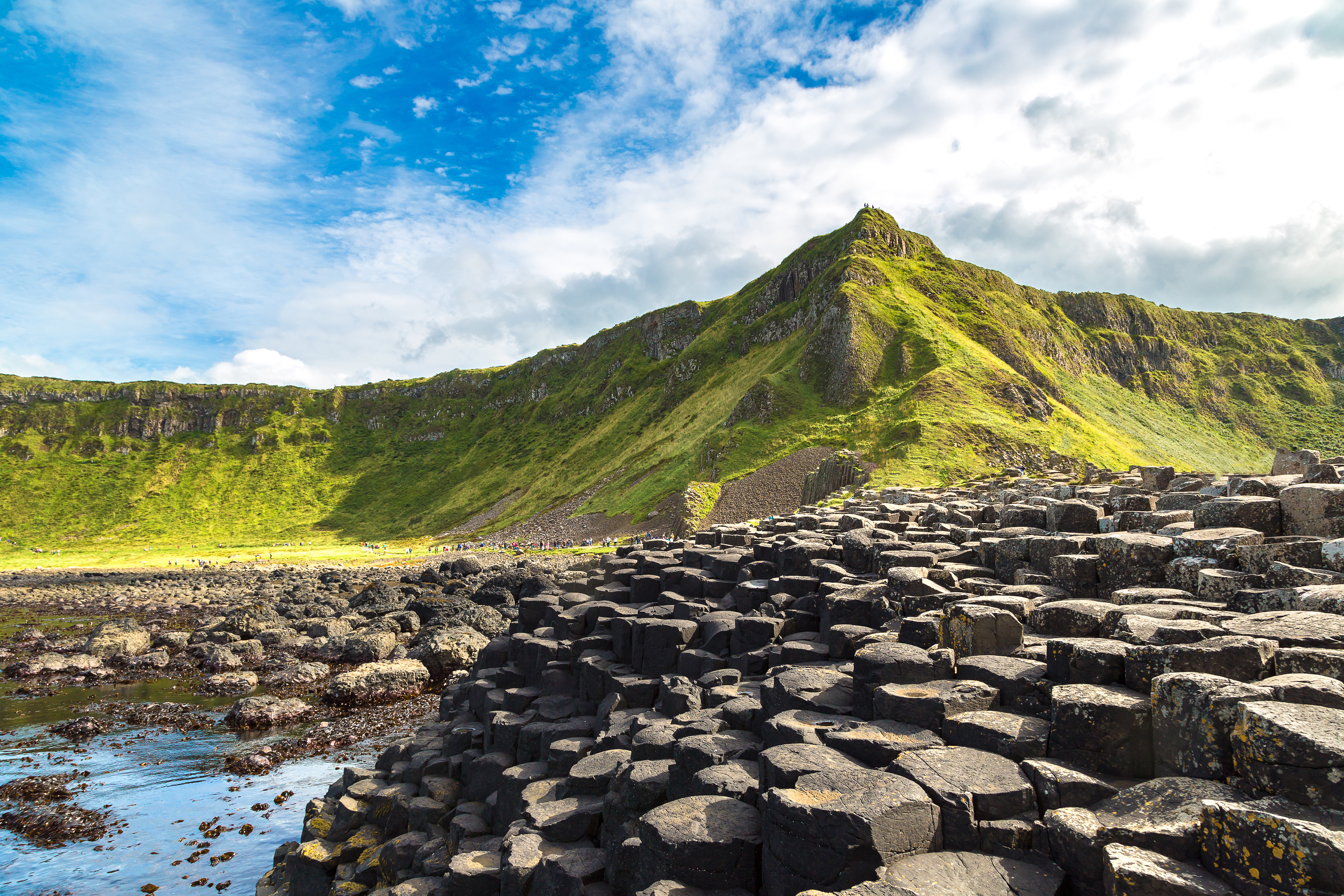 Imponerende vulkanske basaltsøjler ved Giants Causeway kysten i Nordirland med frodige grønne bjerge i baggrunden