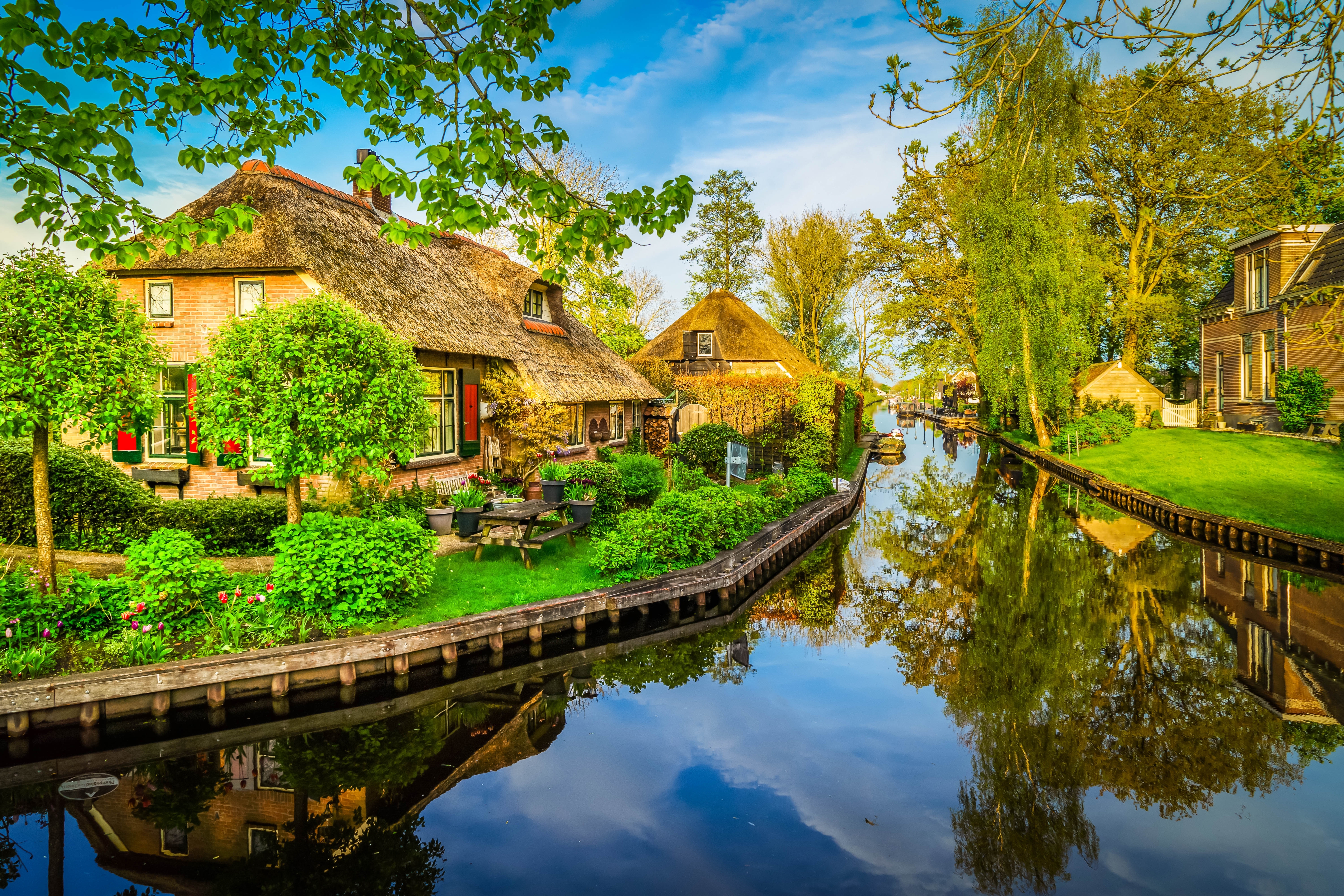 Smukt kanallandskab i Giethoorn, Holland, med rustikke stråtækte huse, frodige haver og rolige vandrefleksioner på en skyfri sommerdag