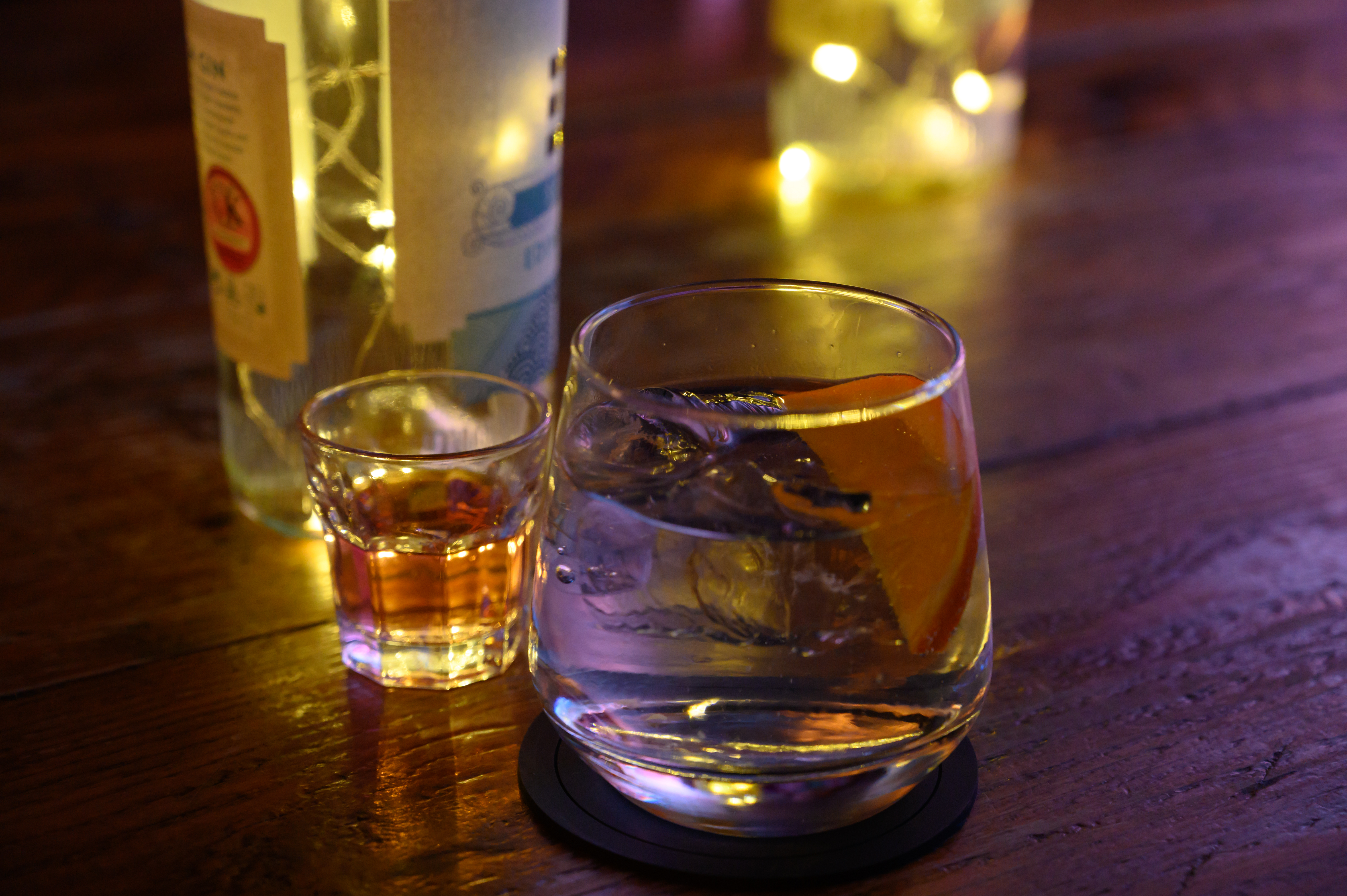 Hyggelig bardrik med gin og tonic på is med appelsin og shot-glas på rustikt træbord med bløde lys i baggrunden