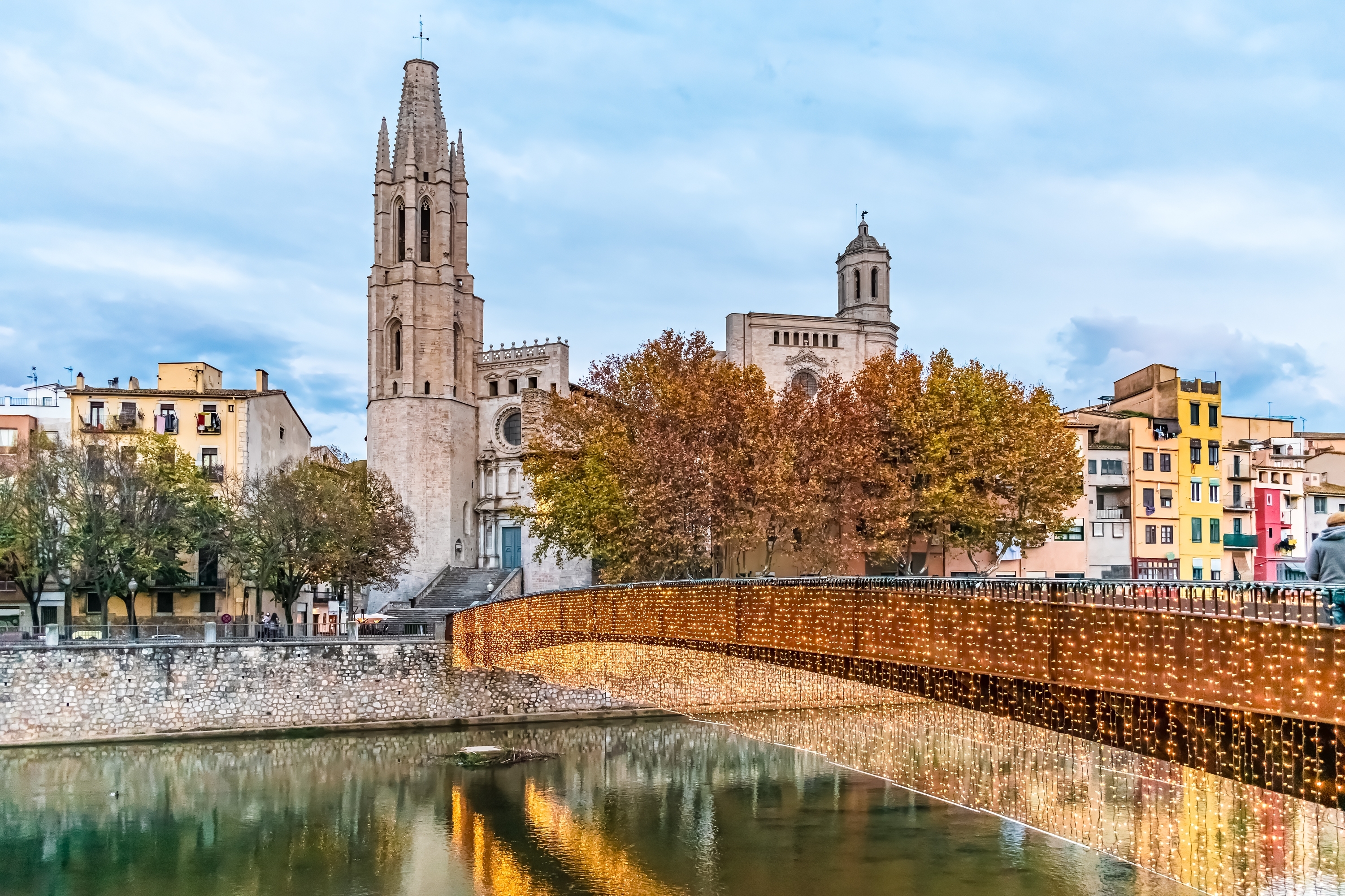 Romantisk vinterbillede af den oplyste Pont de Sant Feliu-bro med julelys og spejlinger i Onyar-floden med farverige huse og gotisk basilika, Girona, Spanien