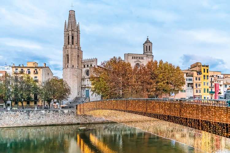 Romantisk vinterbillede af den oplyste Pont de Sant Feliu-bro med julelys og spejlinger i Onyar-floden med farverige huse og gotisk basilika, Girona, Spanien