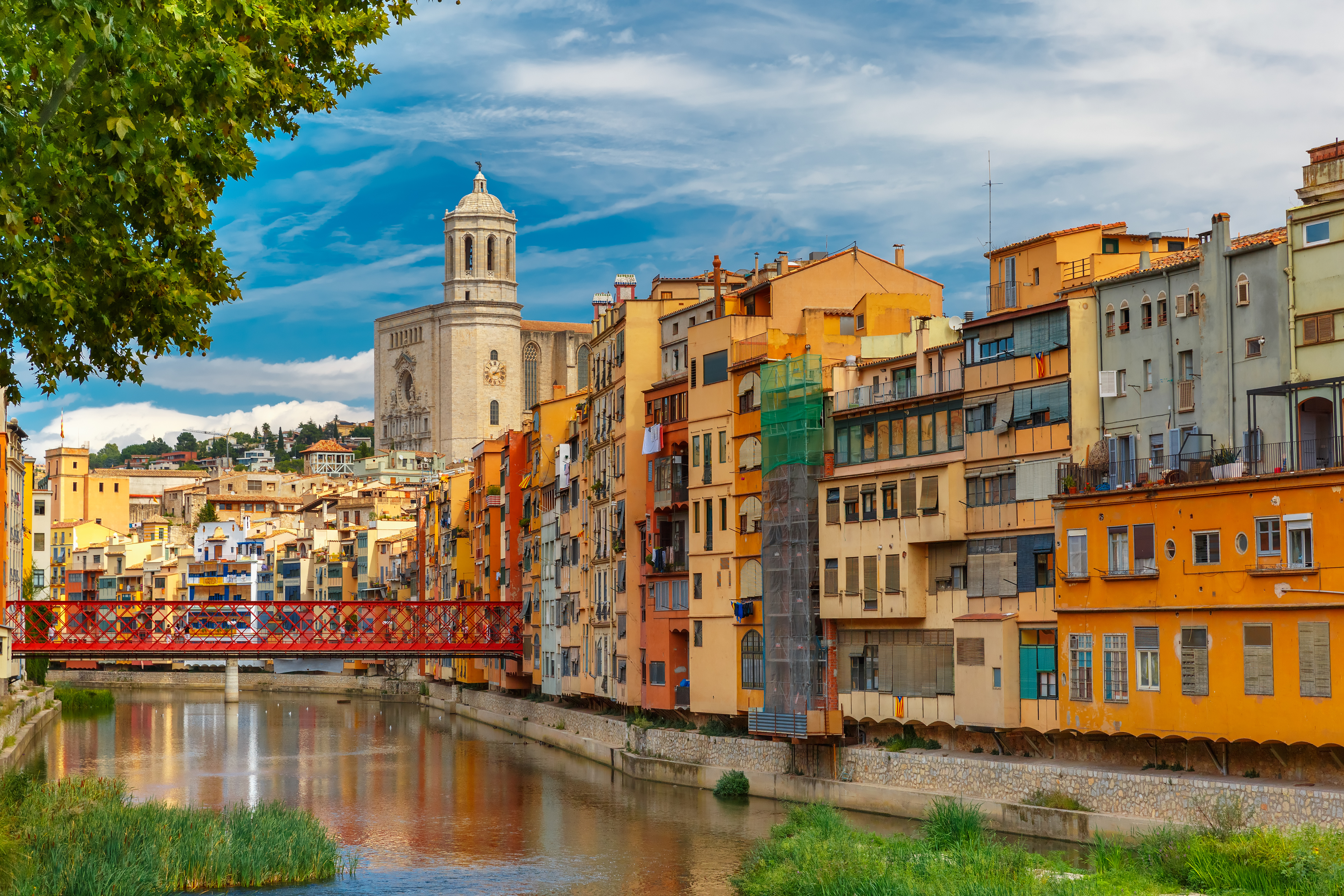 Smukke farverige huse langs Onyar-floden i Girona med den karakteristiske røde bro og katedralen i baggrunden, Spanien